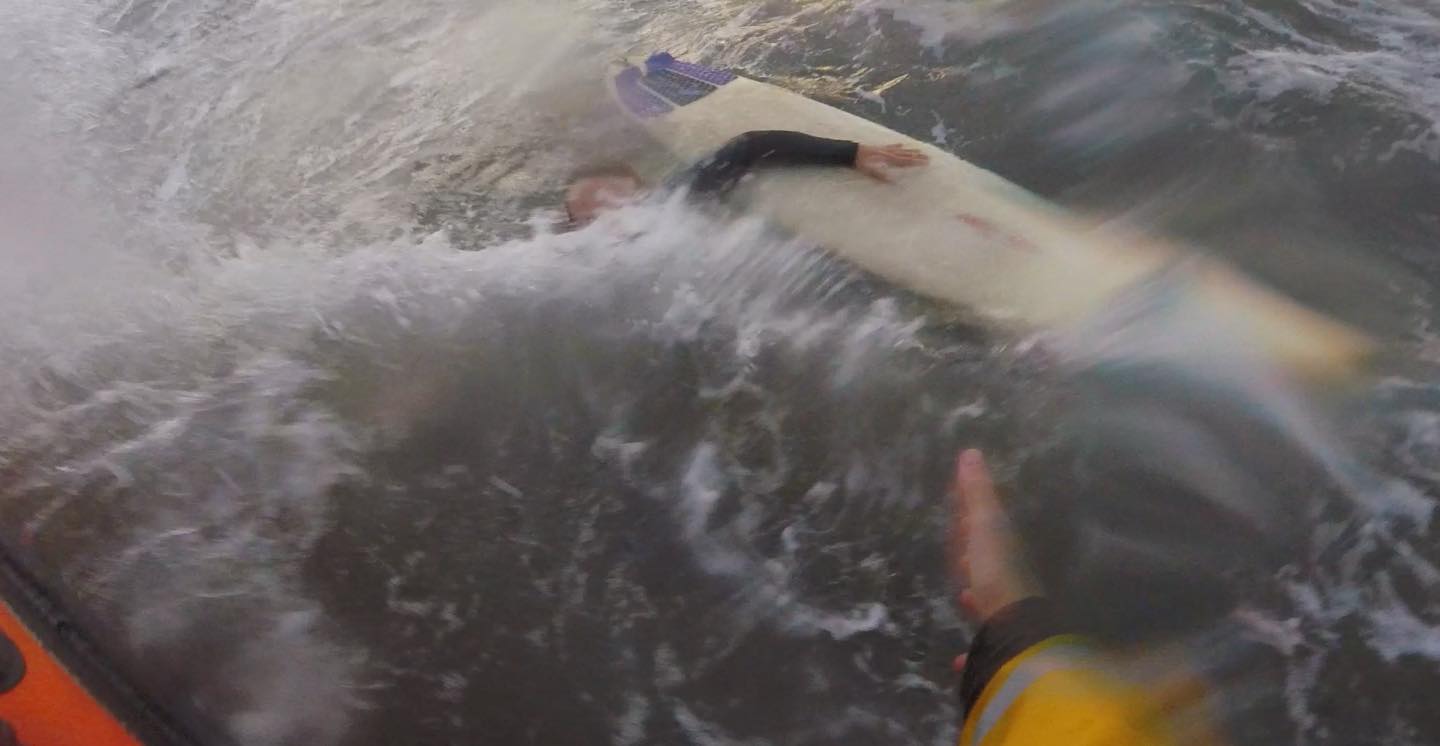 Choppy water going over surfer's head as lifeboat approaches. 