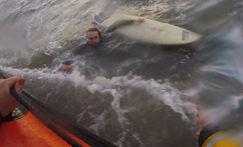 Surfer holding onto surfborad as lifeboat approaches.