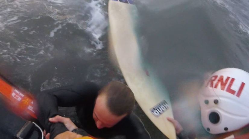 surfer being pulled into lifeboat by crew members.