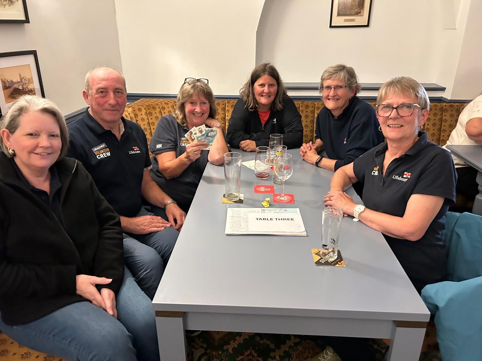 male and female memebers of Wells RNLI in branded clothing sat posed for a photo at a Dabbling Duck quiz night
