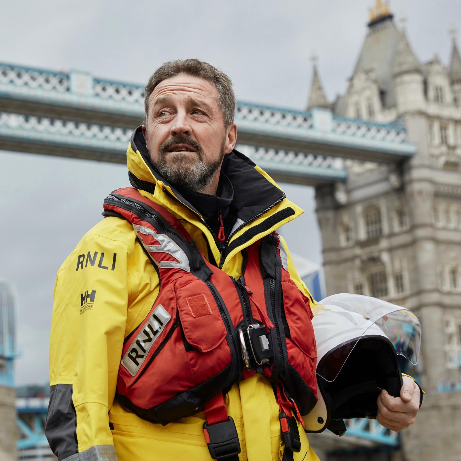 Andy Merry standing in his yellow PPE in front of Tower Bridge with a serious off the shoulder pose.