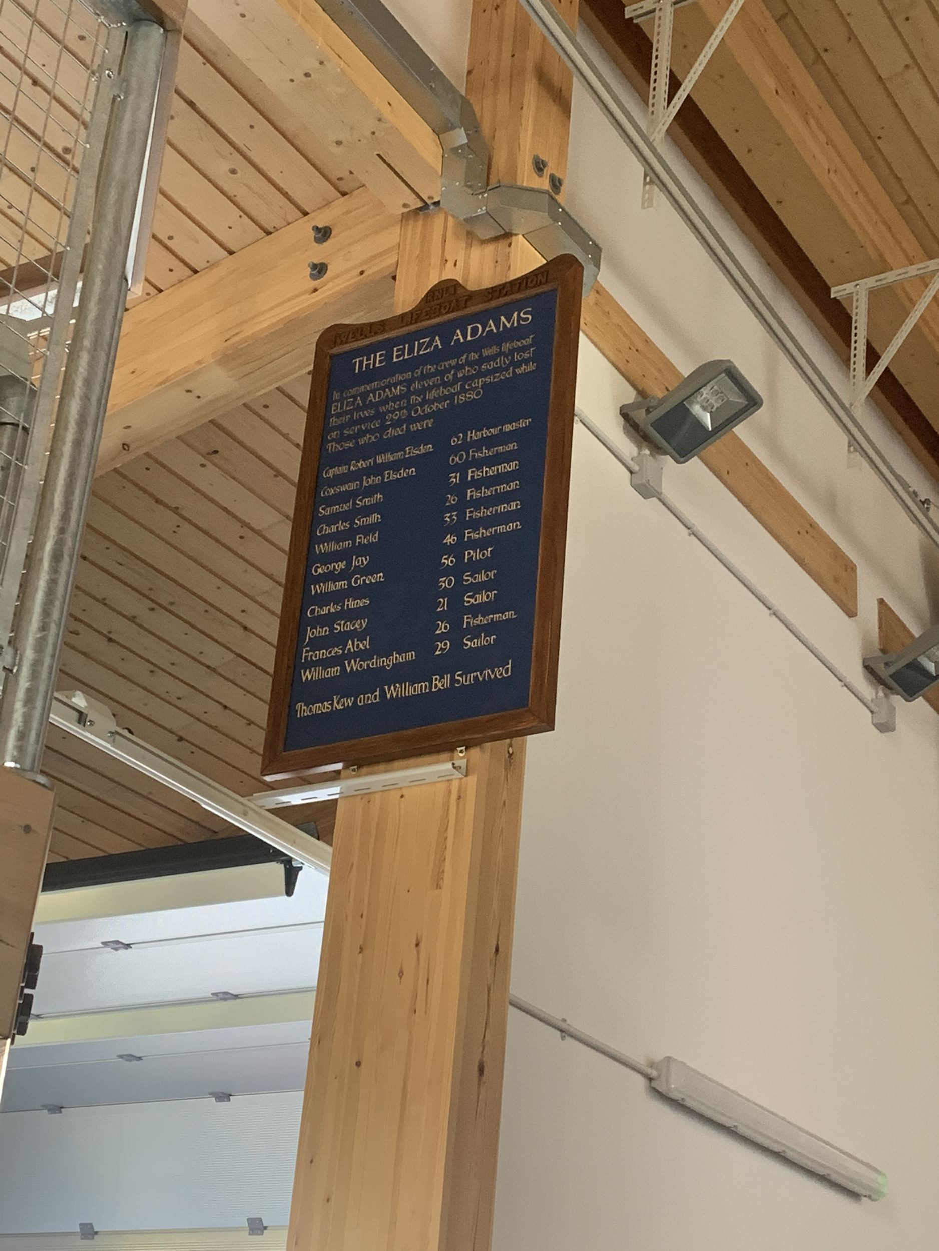 Memorial service board in Wells RNLI boathouse in honour of the Eliza Adams crew. Service board in memory of the Eliza Adams crew, wooden board with gold leaf writing on a blue background

