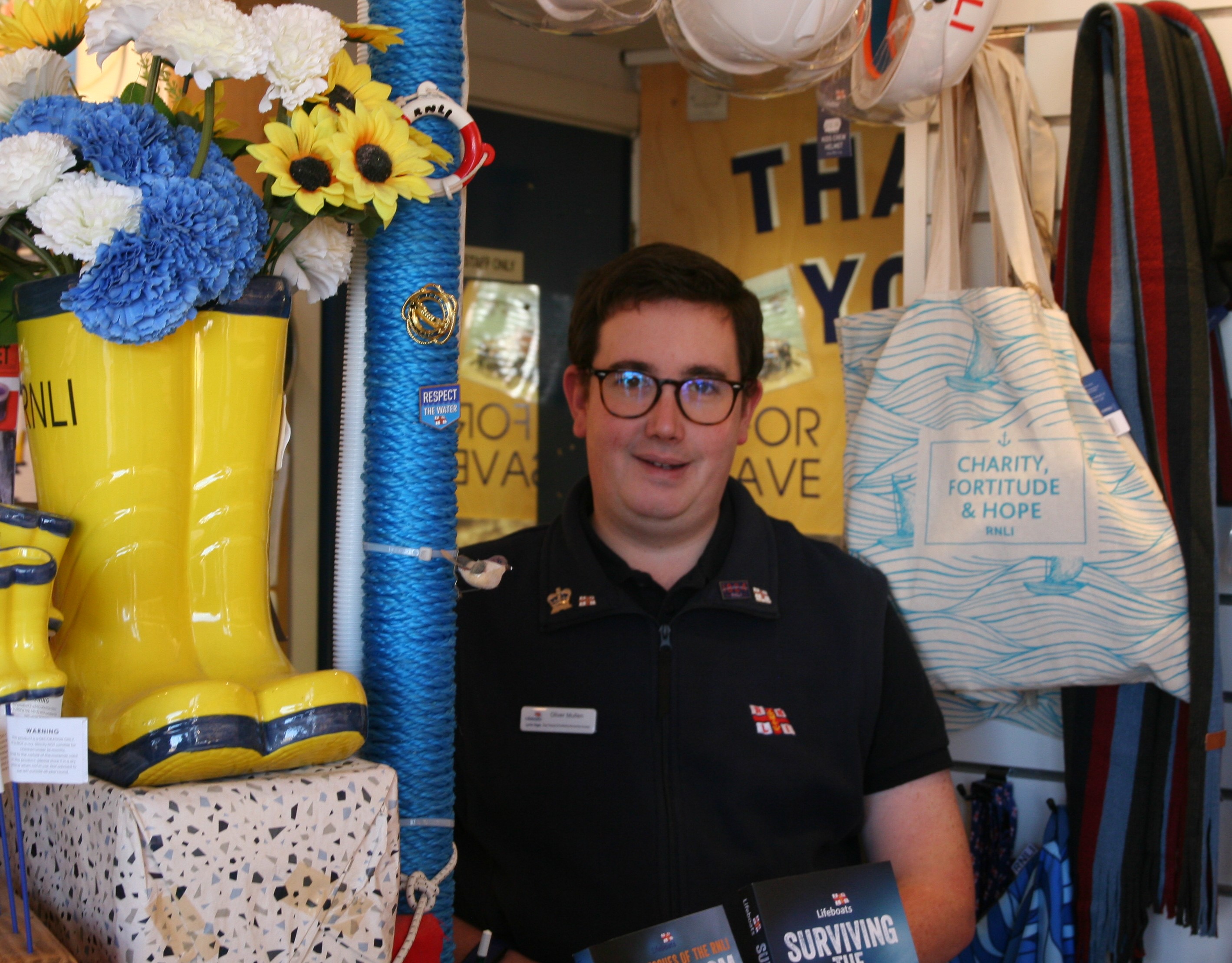 Man in RNLI top surrounded by RNLI merchandise
