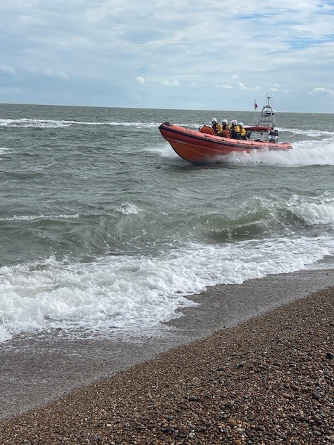 RNLI lifeboat Ralph welcomed to Aldeburgh in official naming ceremony Lifebaot with volunteer crew in water and shingle beach in foreground