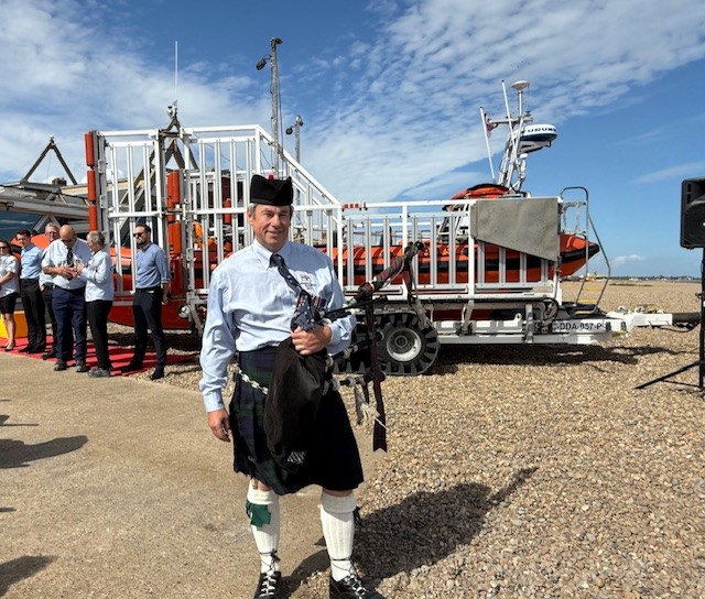 Piper at Aldeburgh RNLI in official naming ceremony. Piper in full uniform with crew and lifeboat behind him

