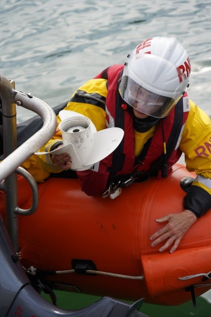 A person lies on the sponson of a lifeboat with a propellor in hand