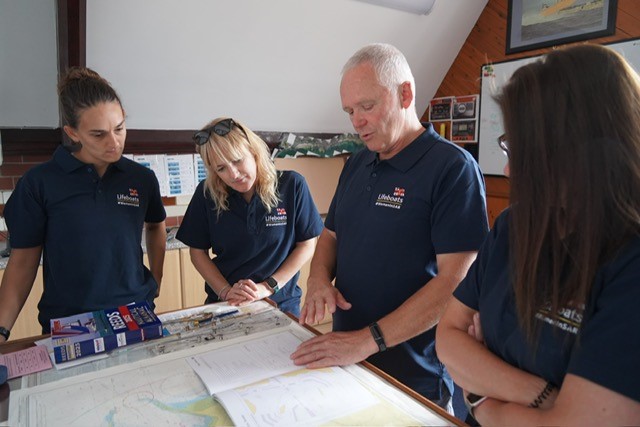 People gather around a nautical chart on a table