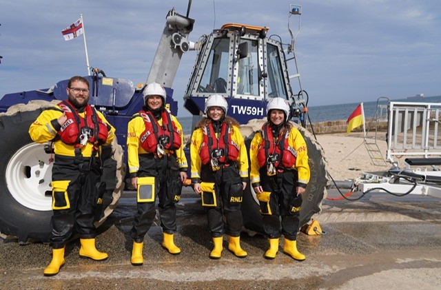 People in drysuits stand in front of an RNLI tractor