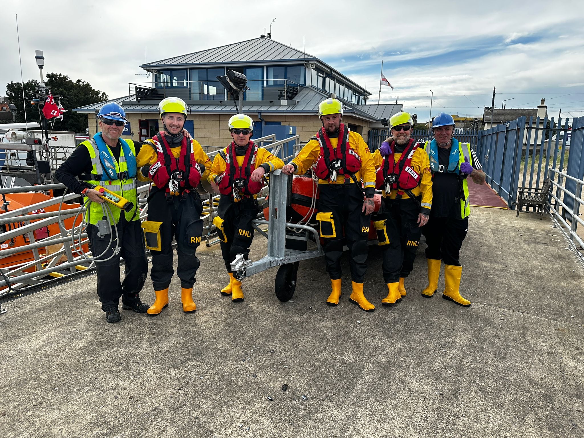 Six members of RNLI Fleetwood's volunteer crew, with Fleetwood Lifeboat Station in the background.
