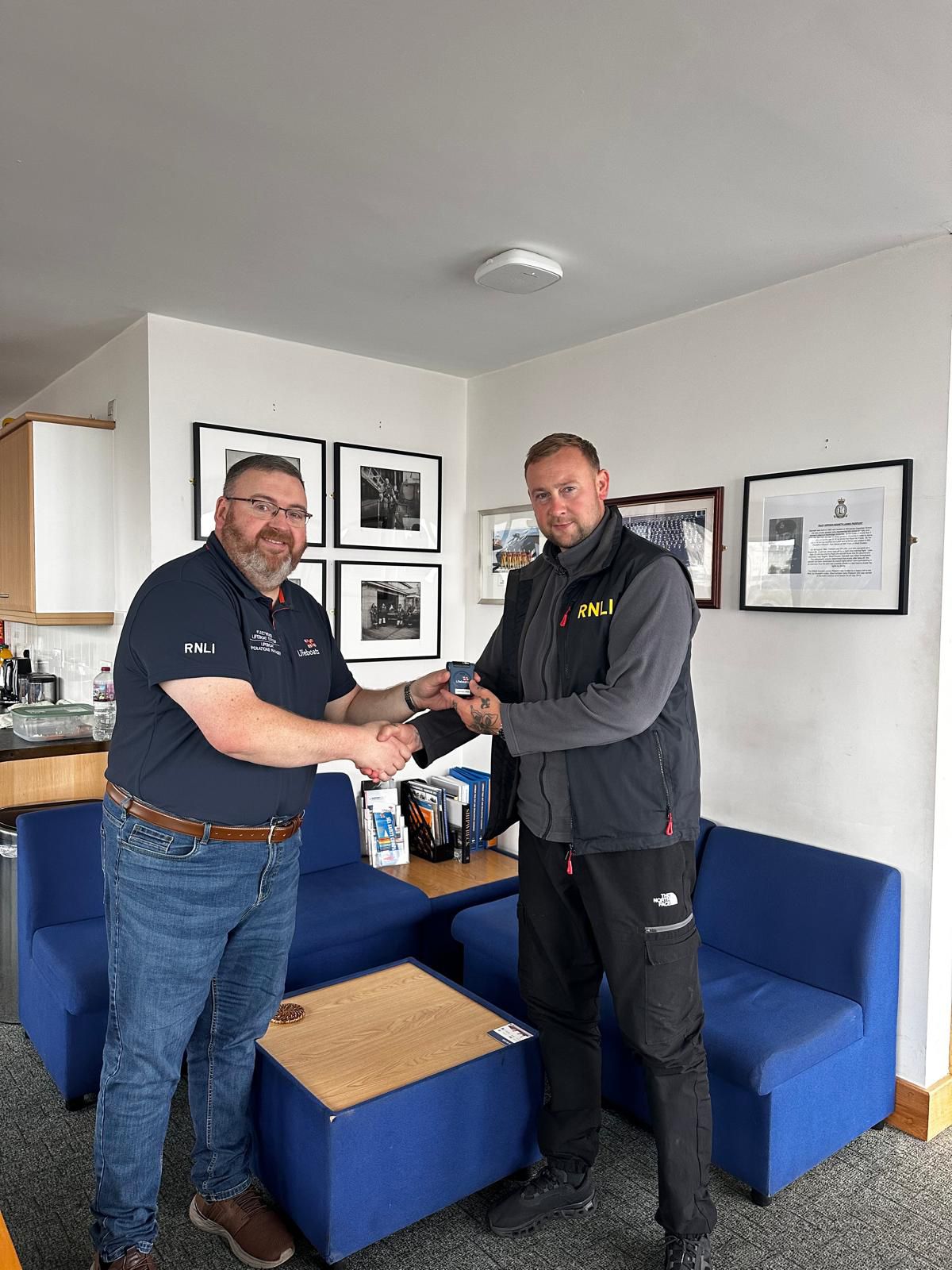 Two men indoors, handing over an RNLI crew pager.