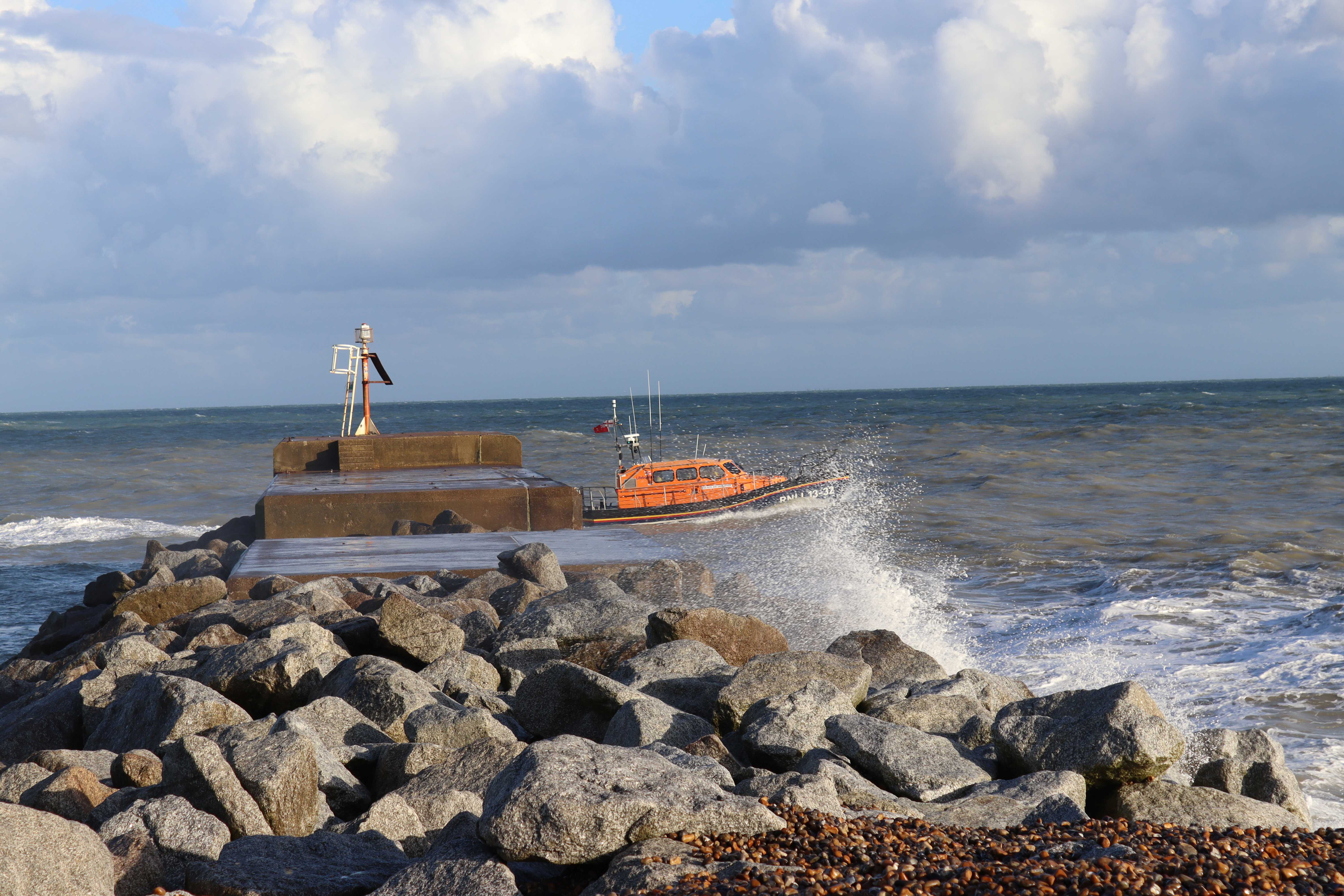 Seaspray breaks over the harbour arm as the lifeboat passes
