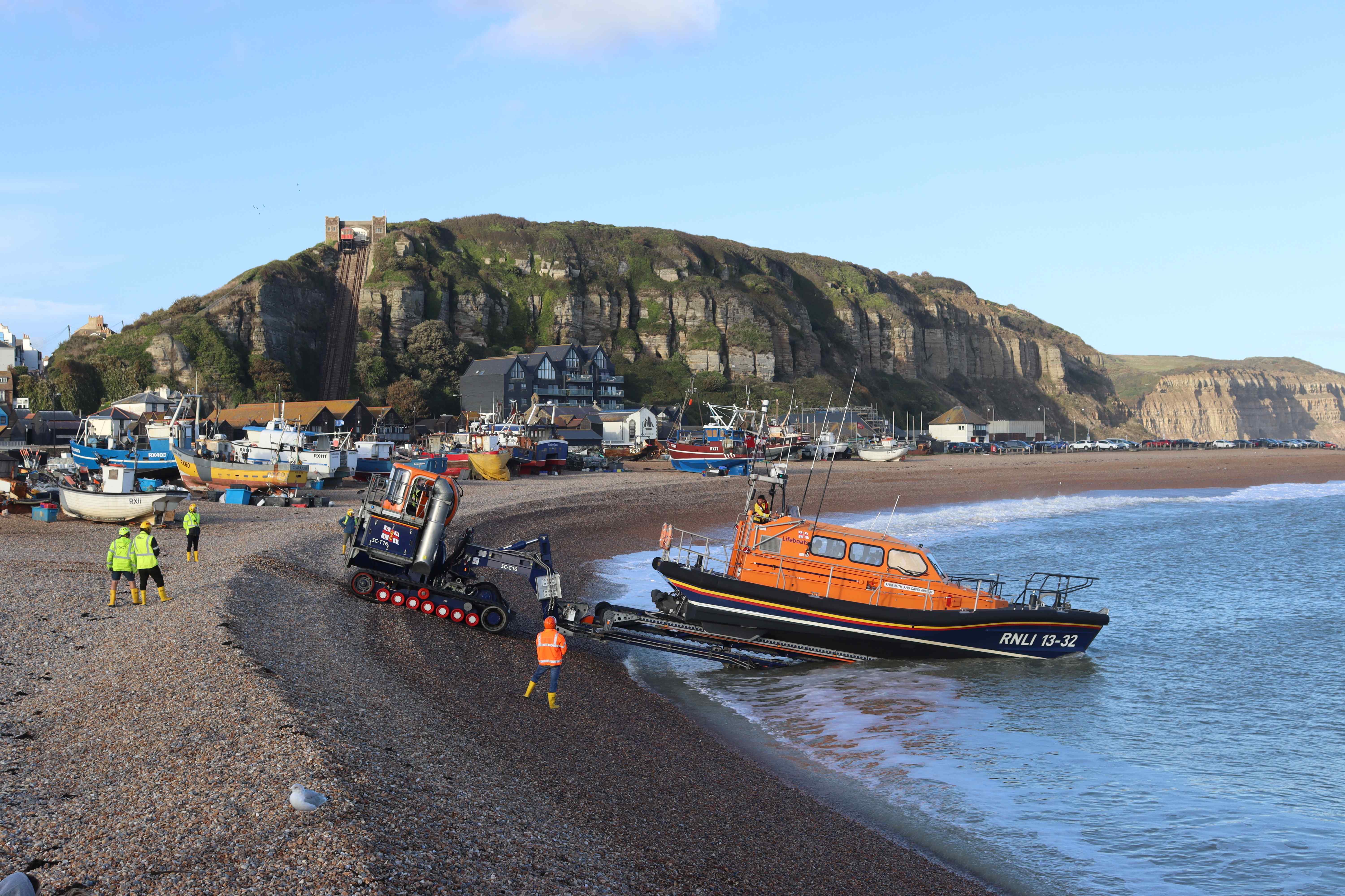 The lifeboat is launched into the sea, with a backdrop of fishing boats and cliffs