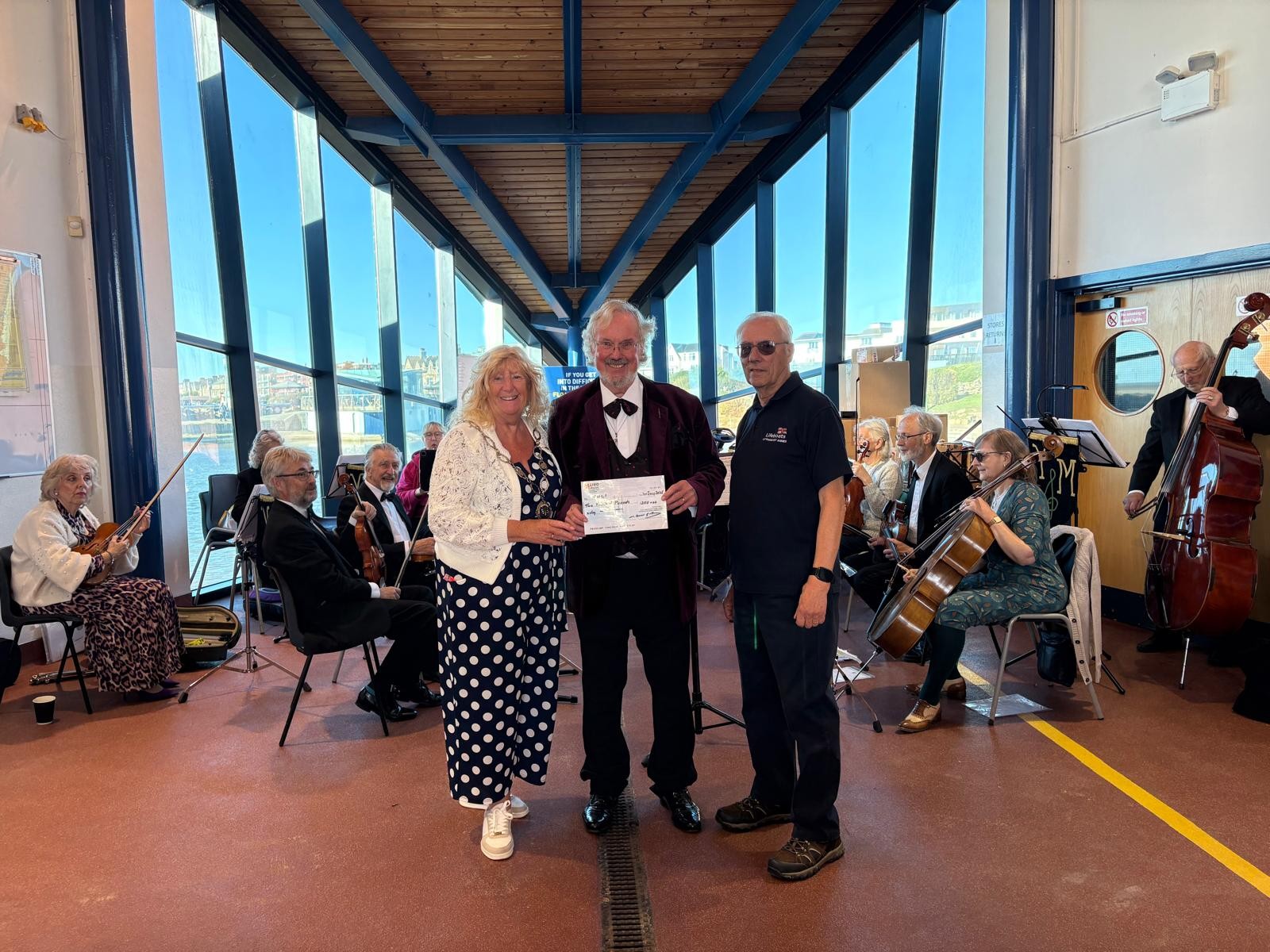 a cheque is being presented with the Orchestra in the background