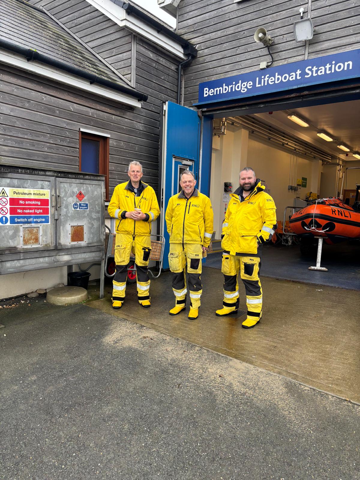 Three crew in RNLI uniform outside inshore lifeboat station looking at the camera
