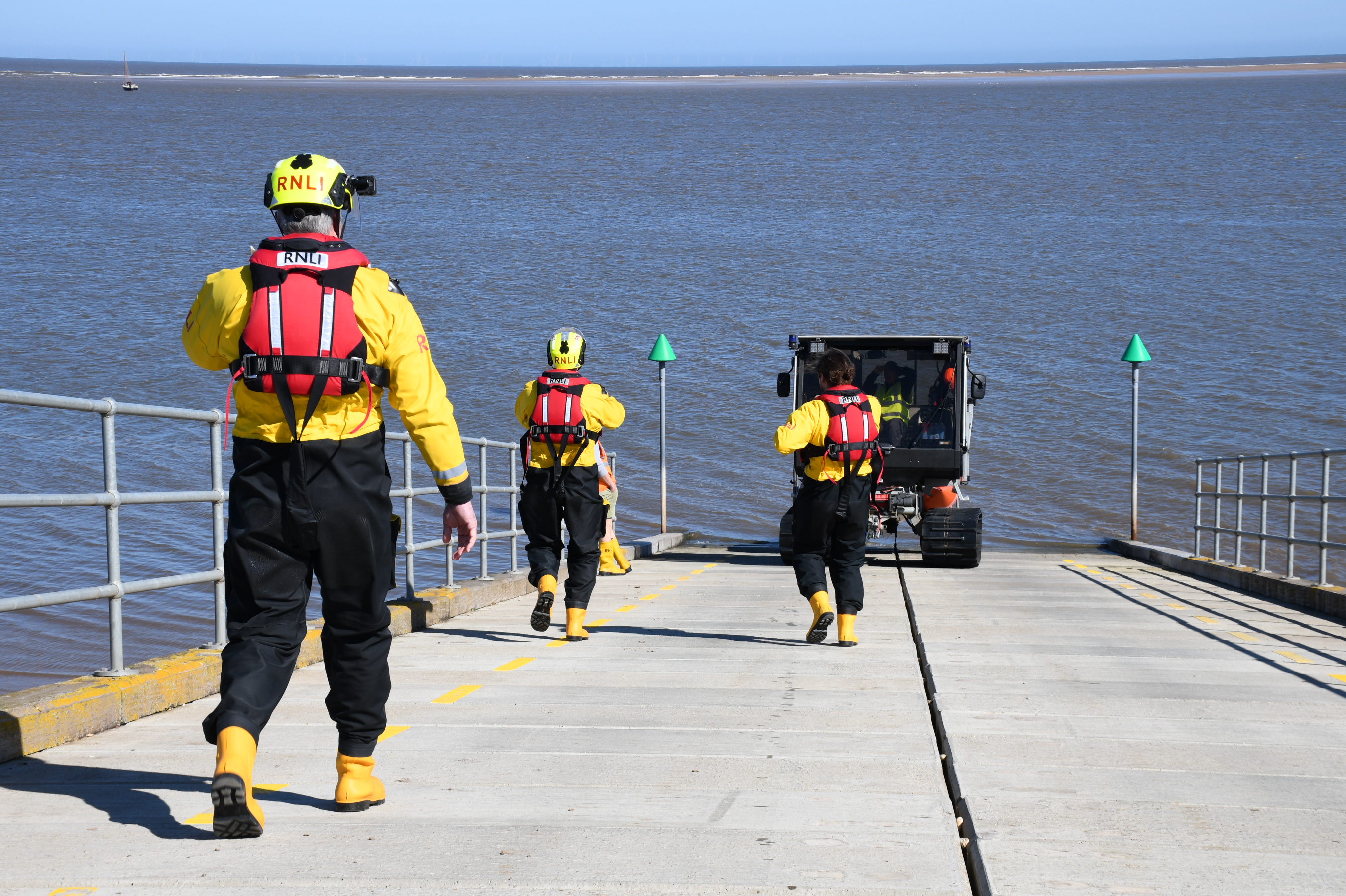 Wells RNLI assist yacht crew ashore after grounding on sands Three RNLI crew heading down the slipway with launch vehicle