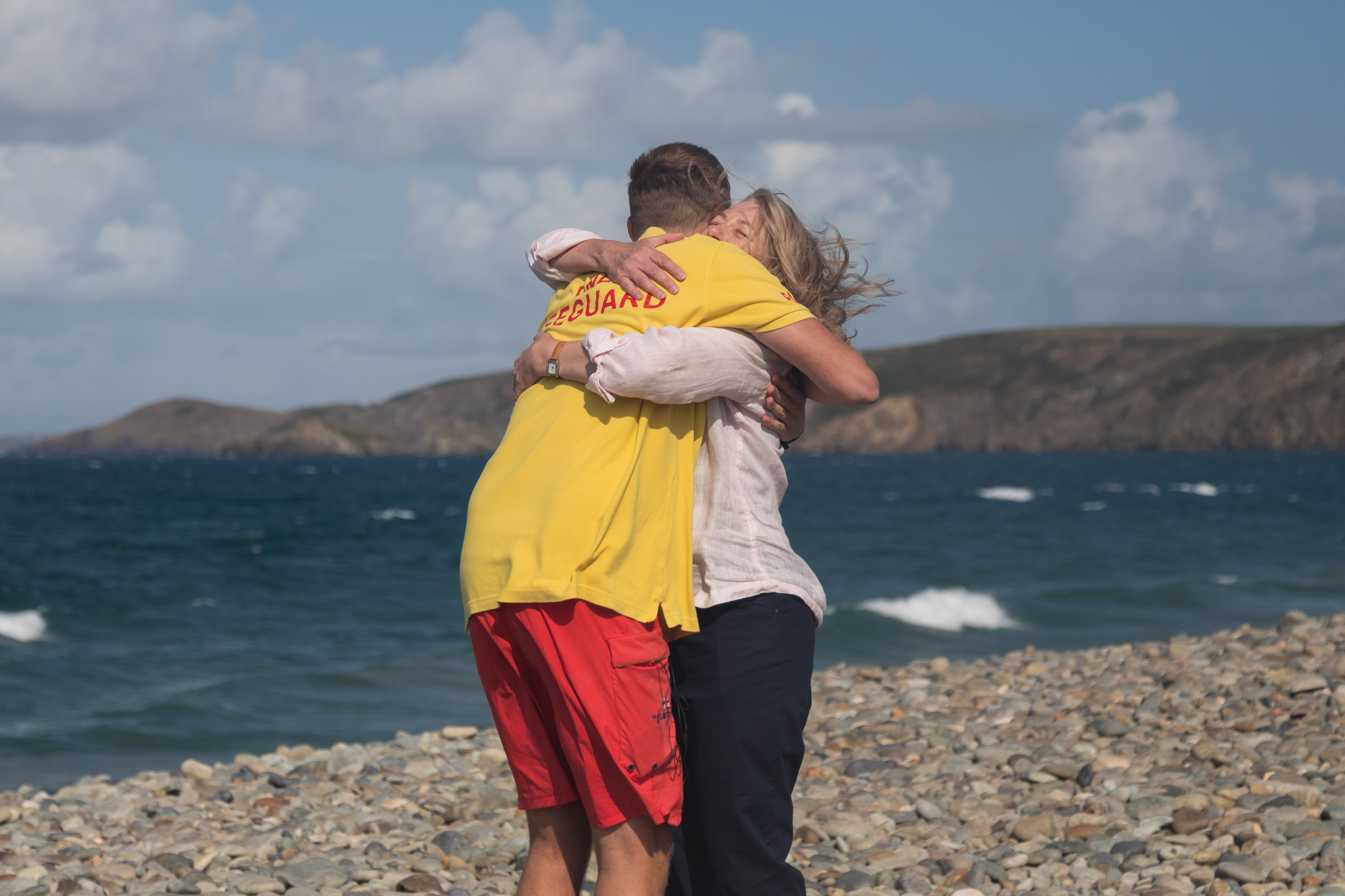 Landscape image of Matty and Joanna embracing a hug when they were reunited at Newgale beach. Sea and headland in the backdrop.