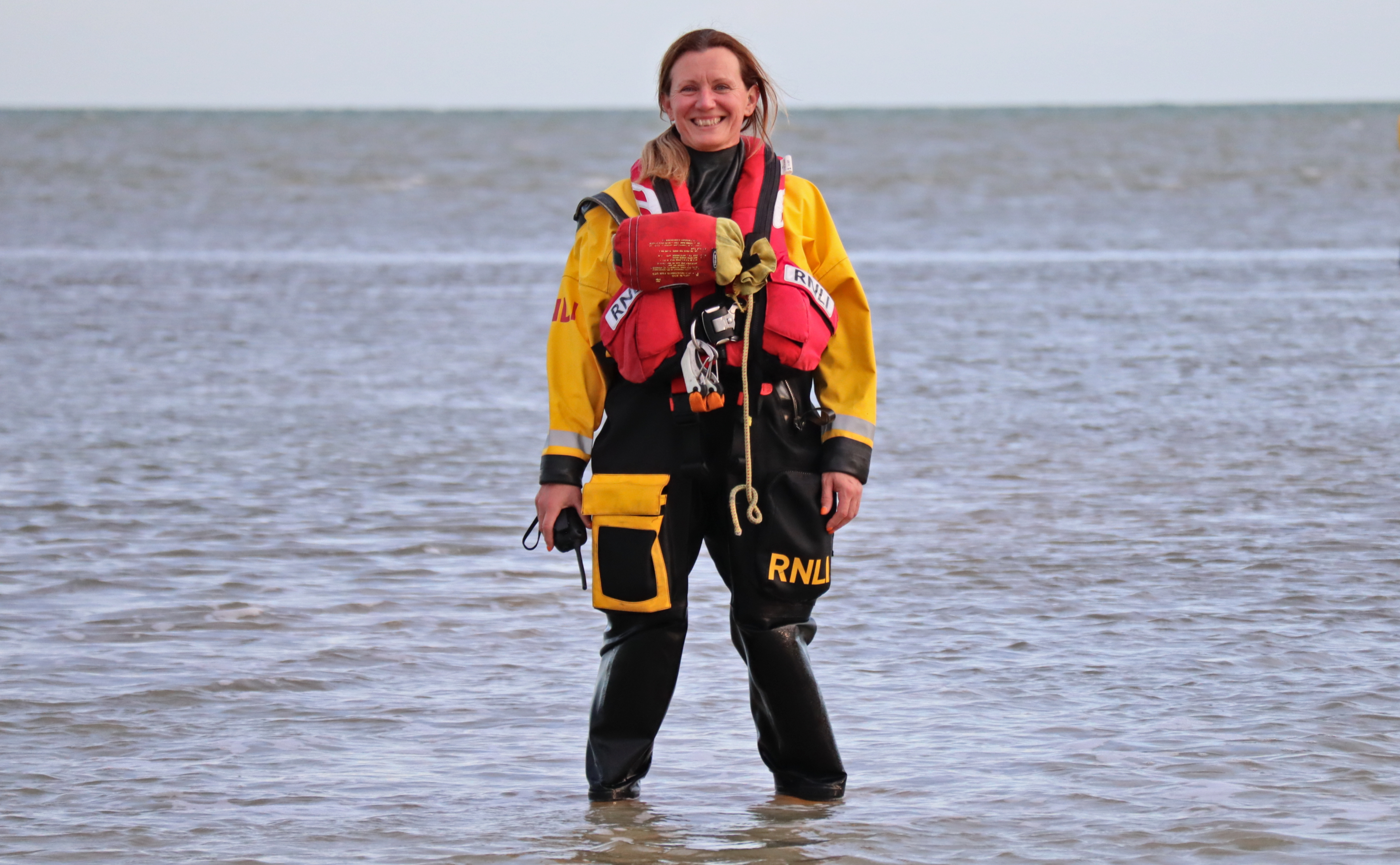 Bea Homer in her crew kit standing ankle-deep in the sea