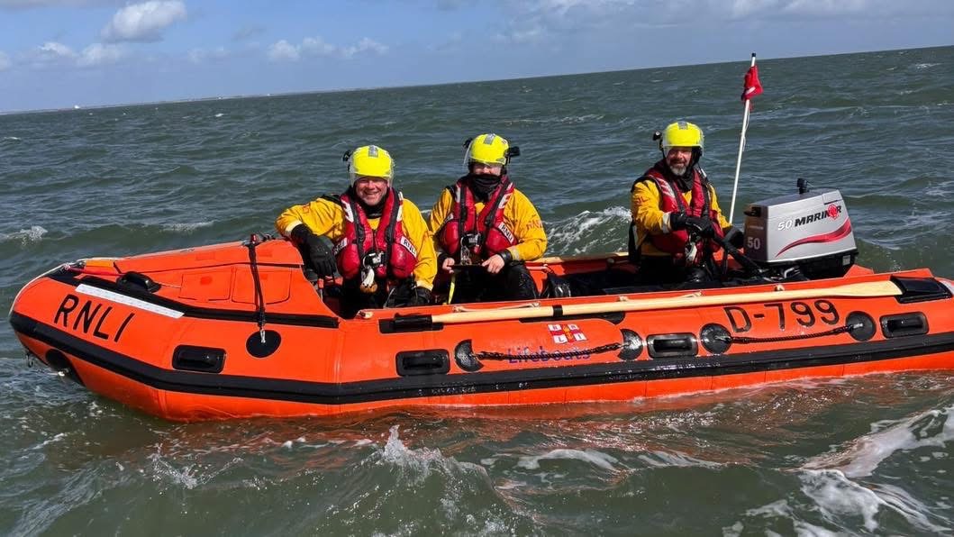 D class lifeboat with three volunteer crew in full RNLI kit and lifejackets on the water calm sea's