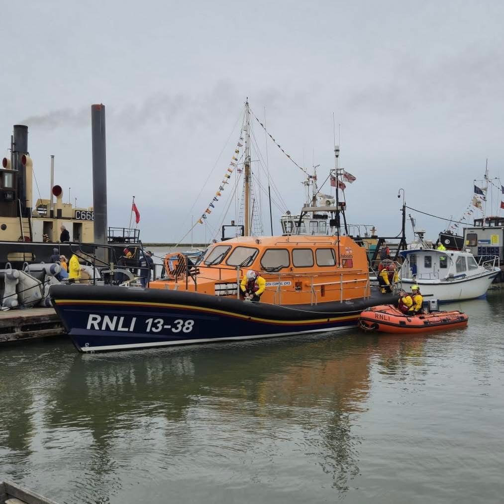 Shannon Class lifeboat with D class beside it in harbour. Other boats in the background and flags