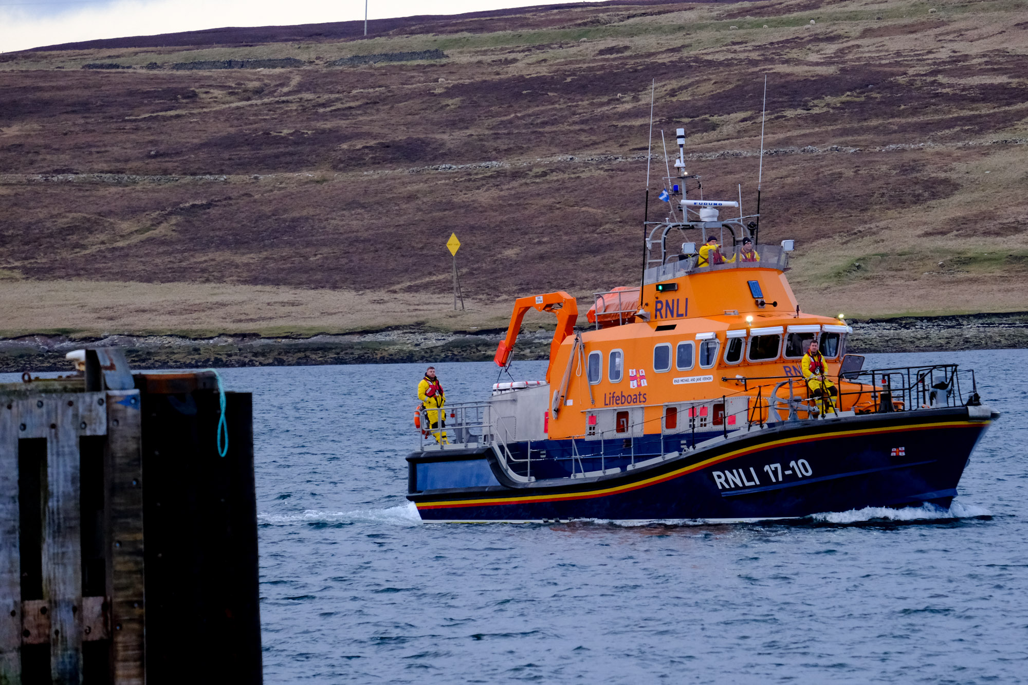 Lerwick Lifeboat on the water, approaching the harbour with crew on deck. 