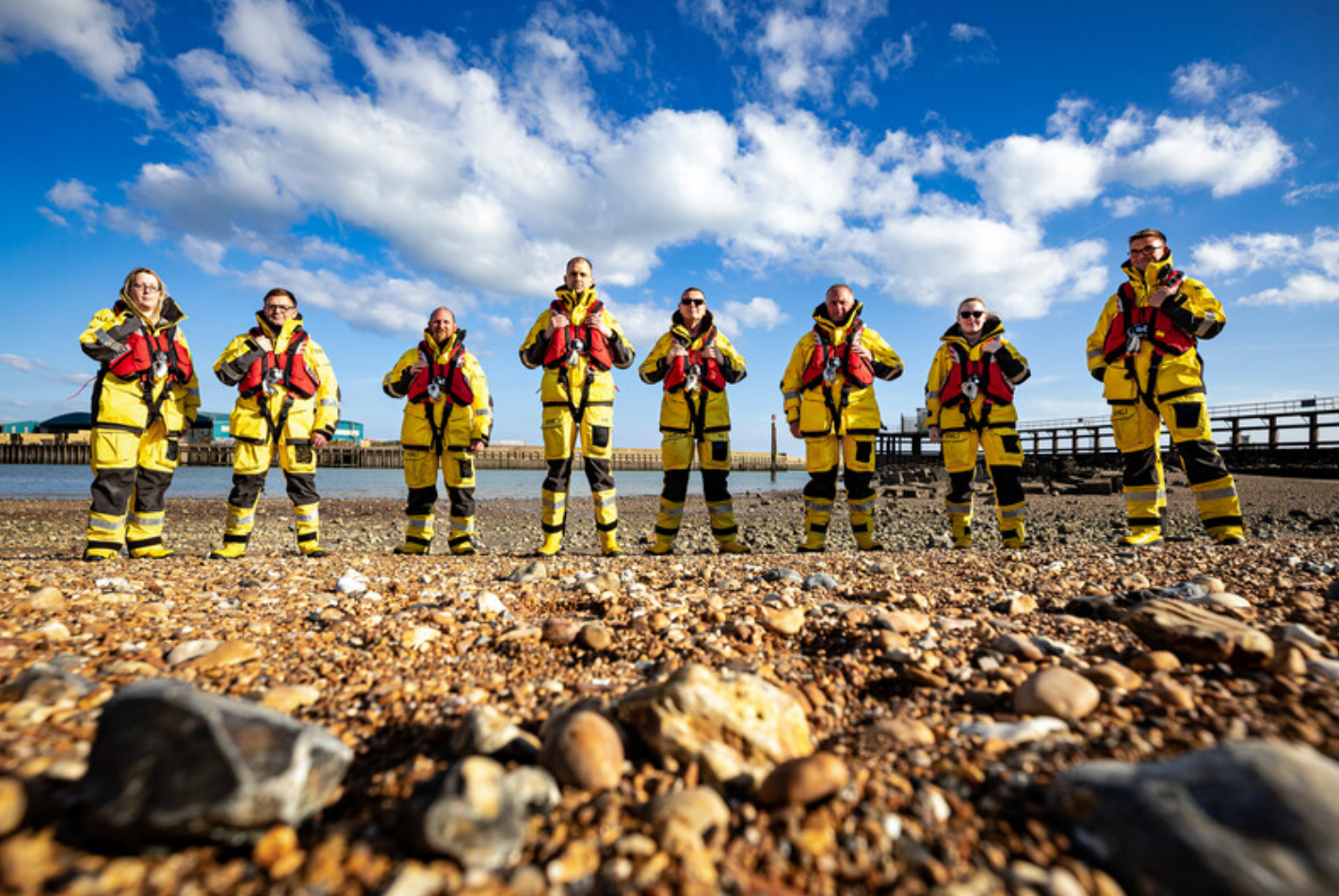 Shoreham RNLI's volunteer crew on the beach on a sunny day. They are wearing their kit.
