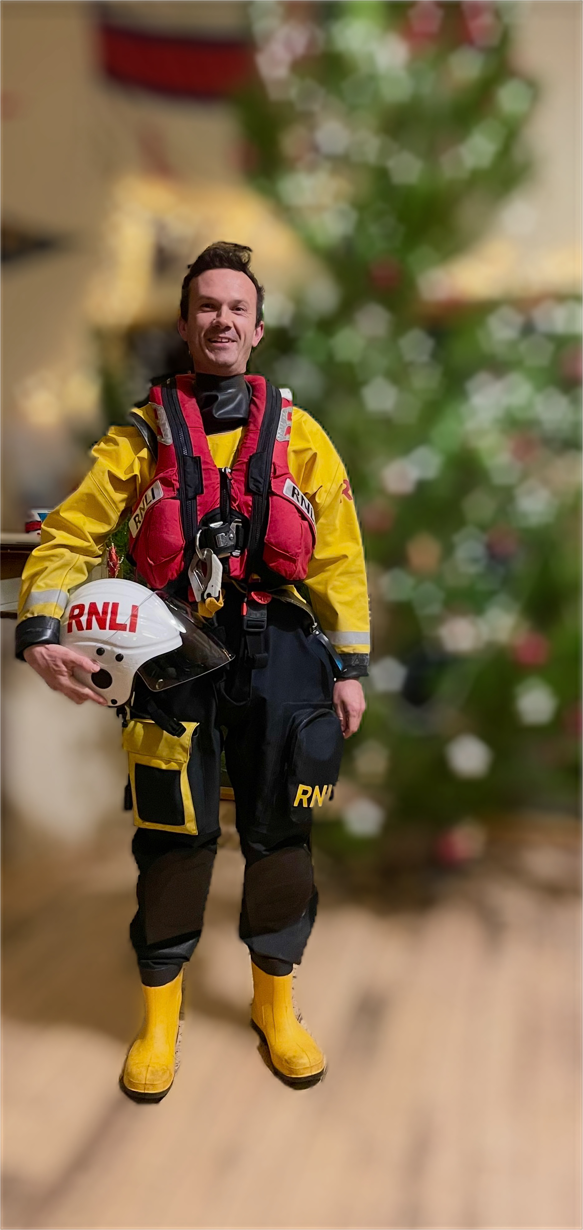 James in full RNLI kit stands smiling at the camera, the background is blurred