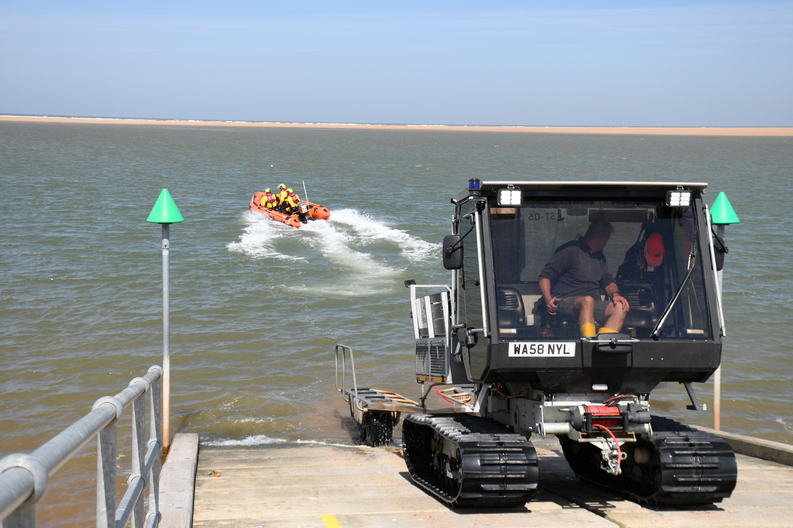 Wells RNLI launches to assist casualty on calm water. Launch vehicle and inshore lifeboat with three volunteers in full RNLI kit