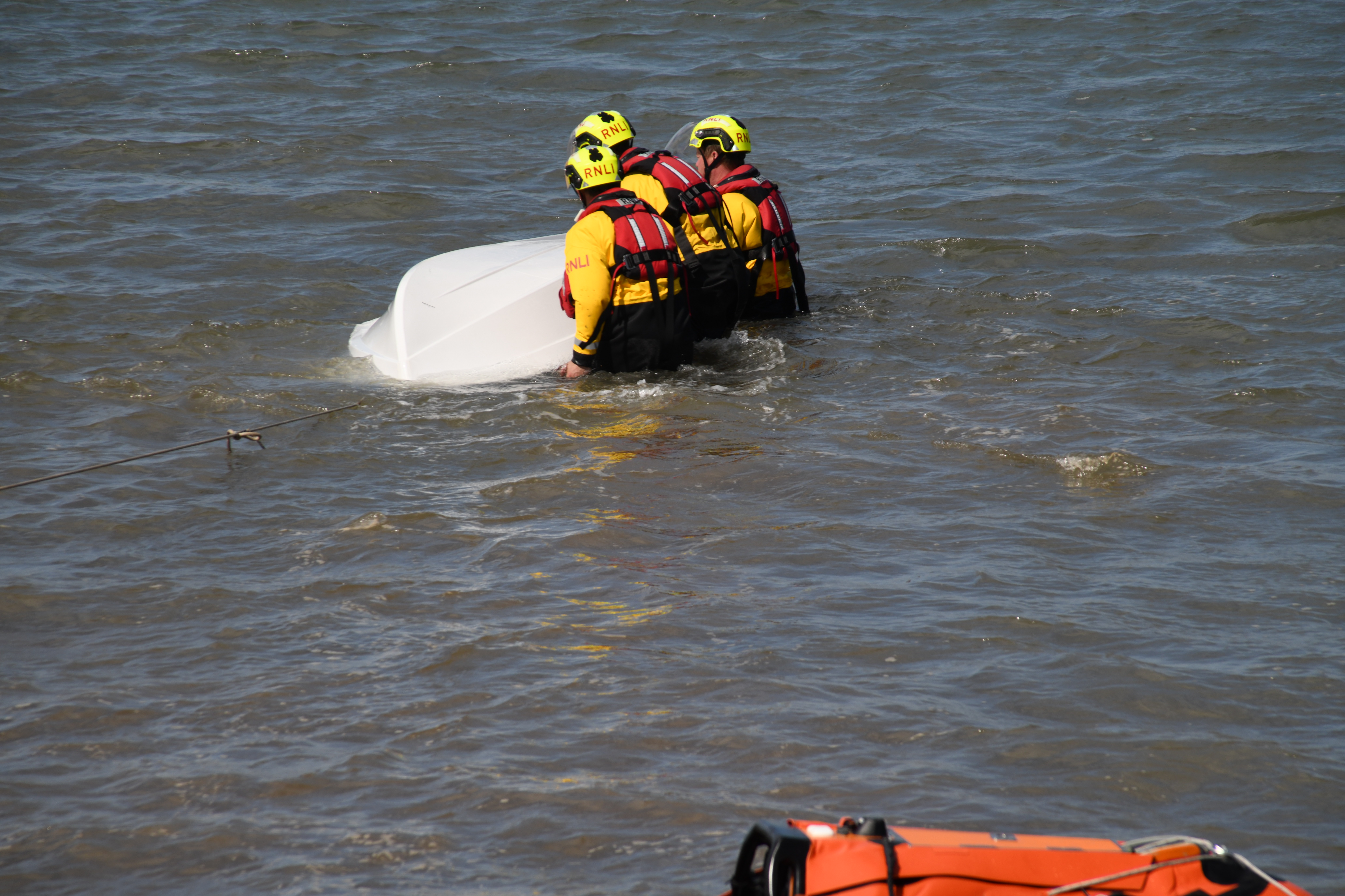 Wells RNLI volunteers in full RNLI kit in the water helping to overturn the vessel