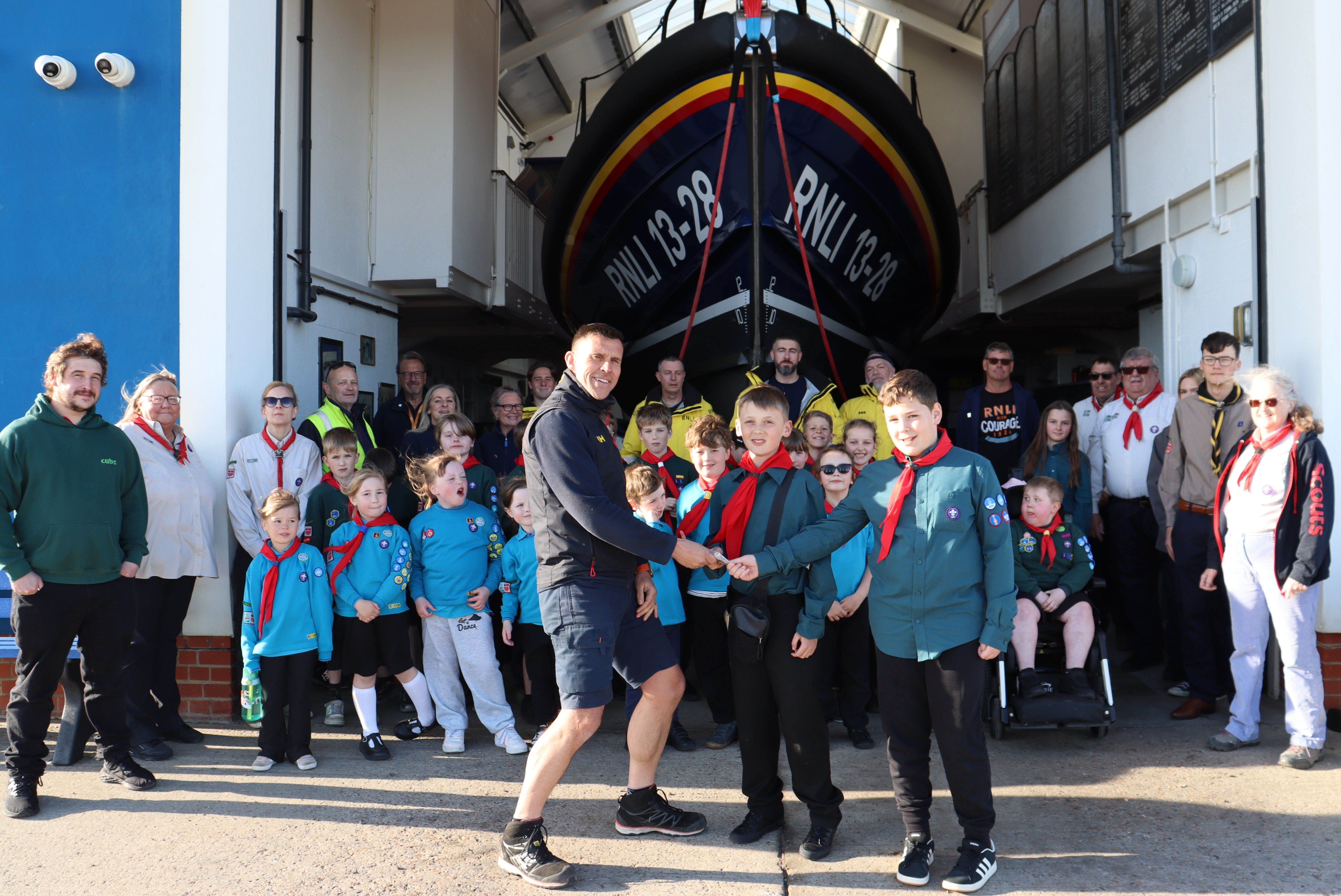 Coxswain Paul McCleery in RNLI clothing accepts money from scouts in uniform, in front of Hastings lifeboat and the rest of the scout group