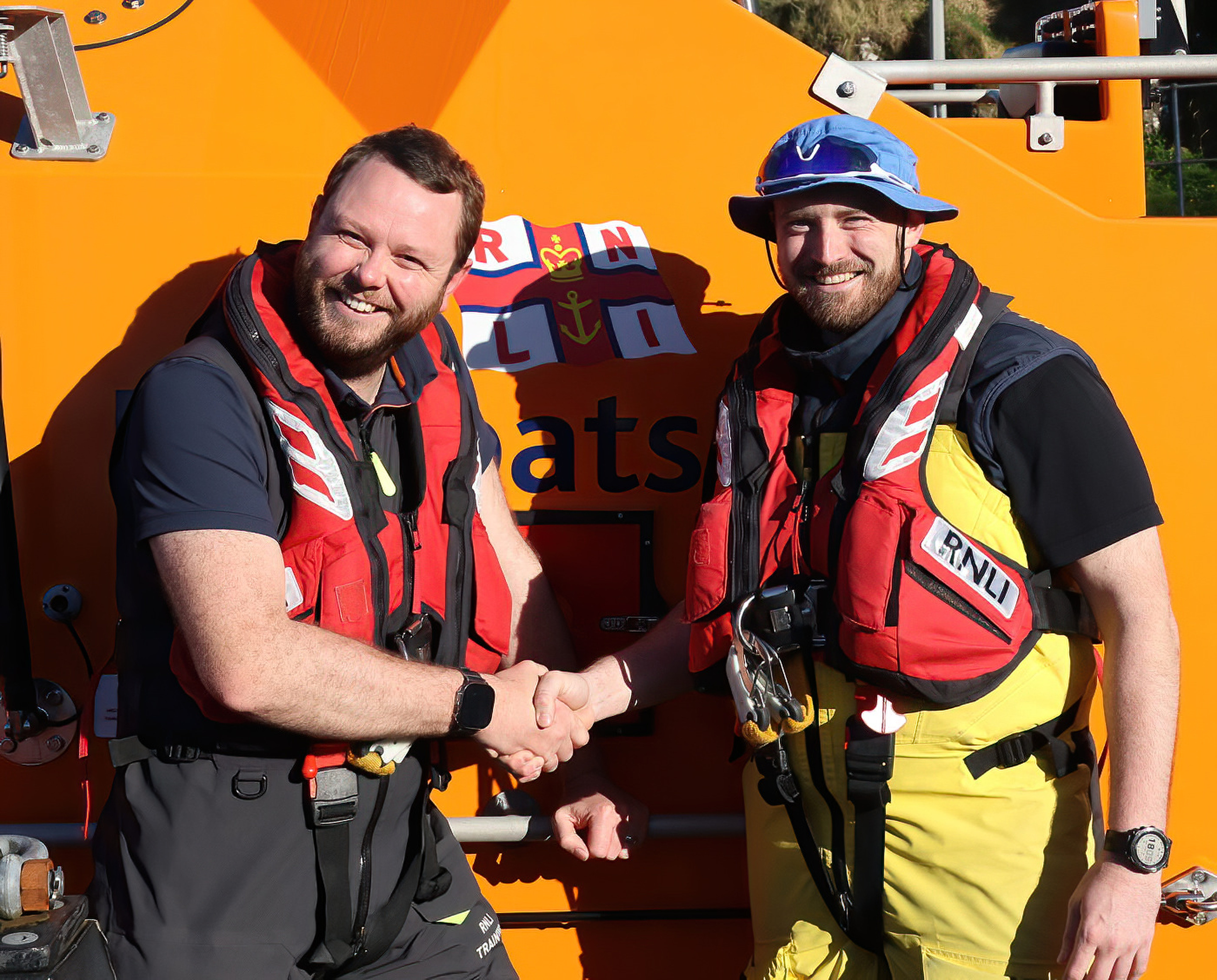 Squinting against the bright sunshine, the new coxswain wearing a sunhat with his full seagoing kit shakes hands with the man who had assessed and ultimately signed him off