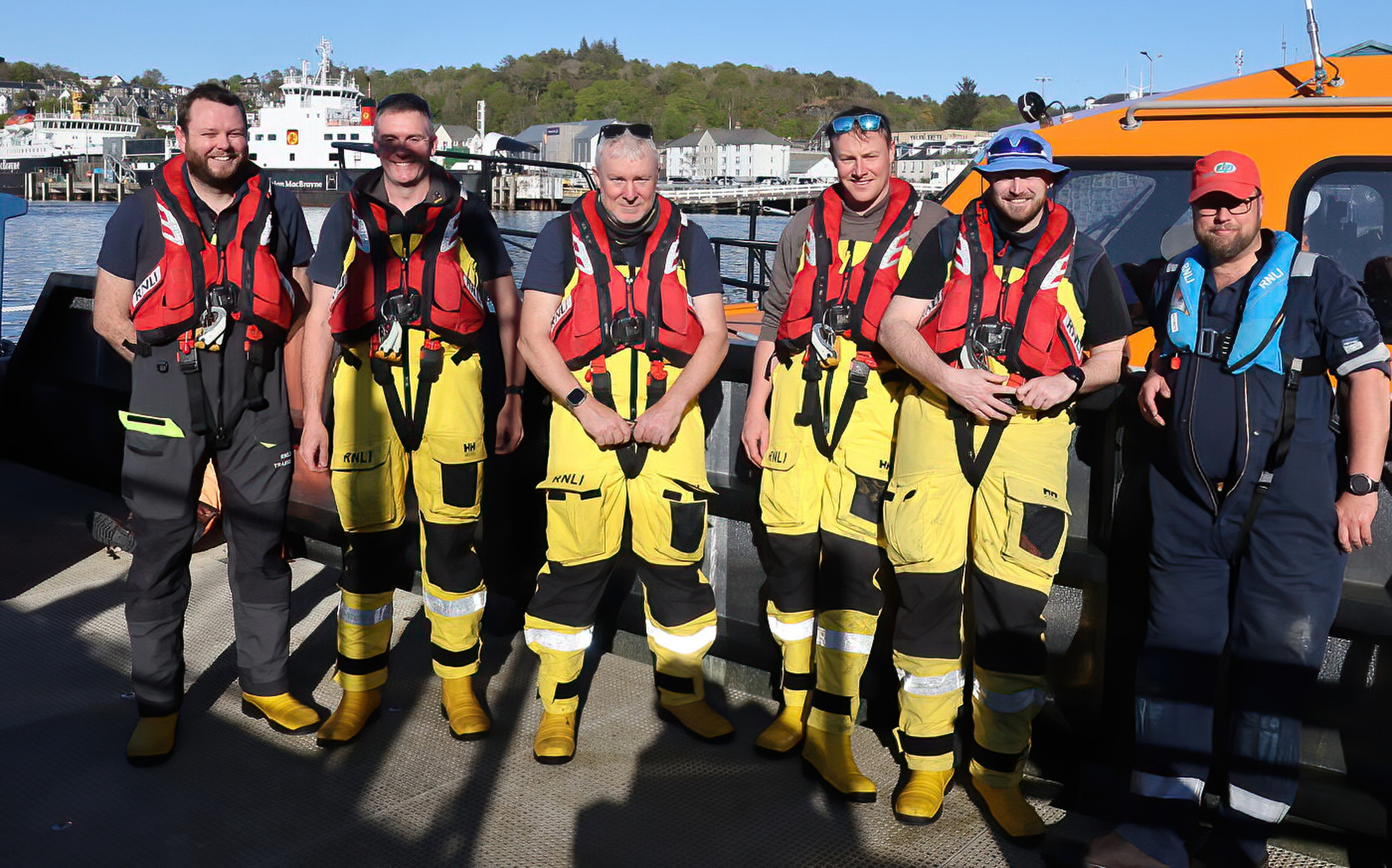 Ruaridh in his sunhat stands alongside five other crew colleagues in front of the Shannon class lifeboat in the sunshine