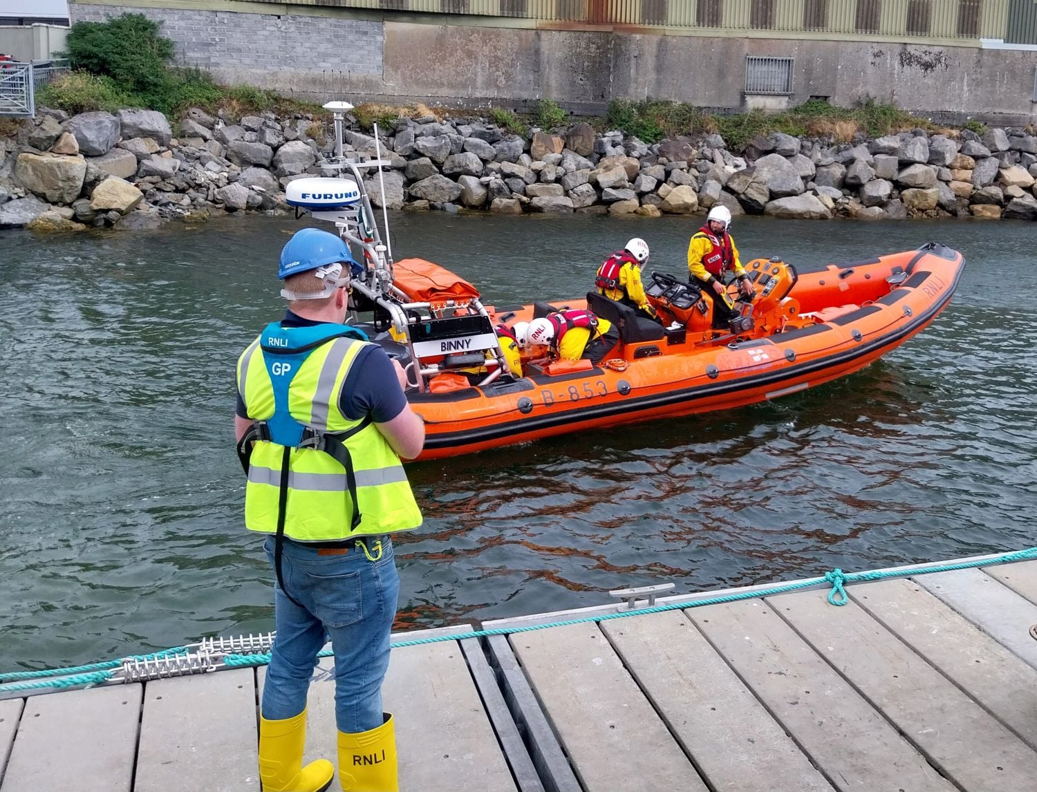 Four crew on board the lifeboat which has just launched with another crew in high vis jacket and lifejacket as shorecrew on the pontoon in the foreground