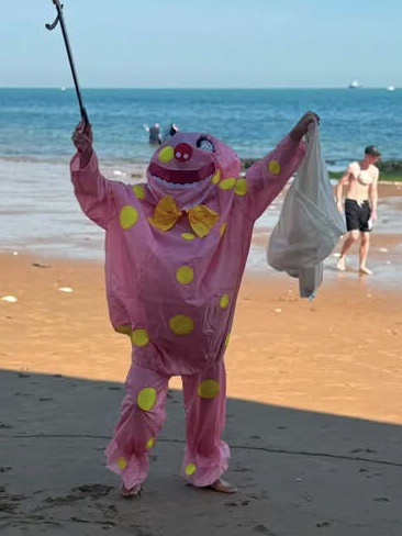 A person in a pink with yellow spots costume standing on a beach.