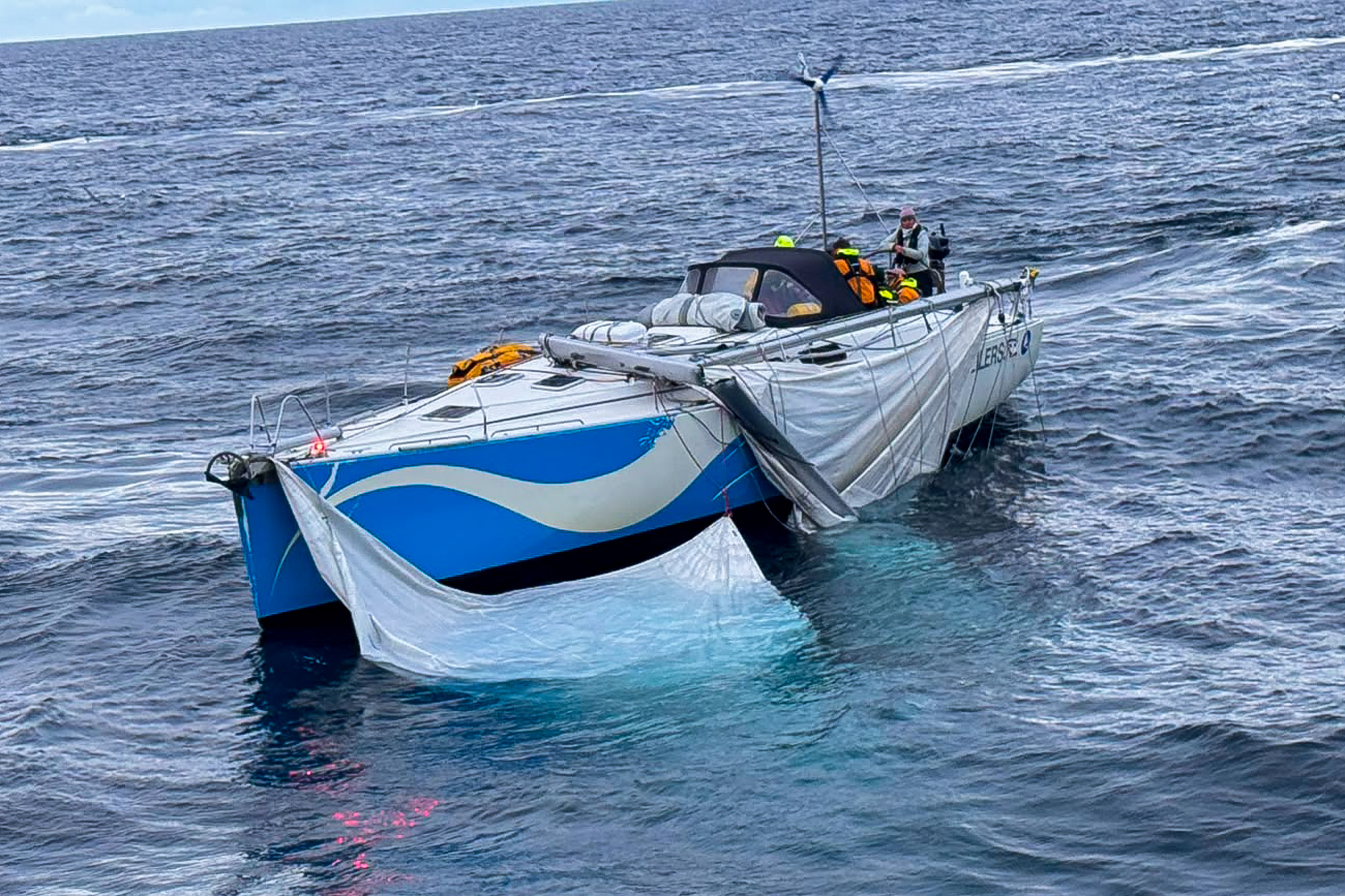 Yacht at sea with a broken main mast, with sails and rigging loose in the water