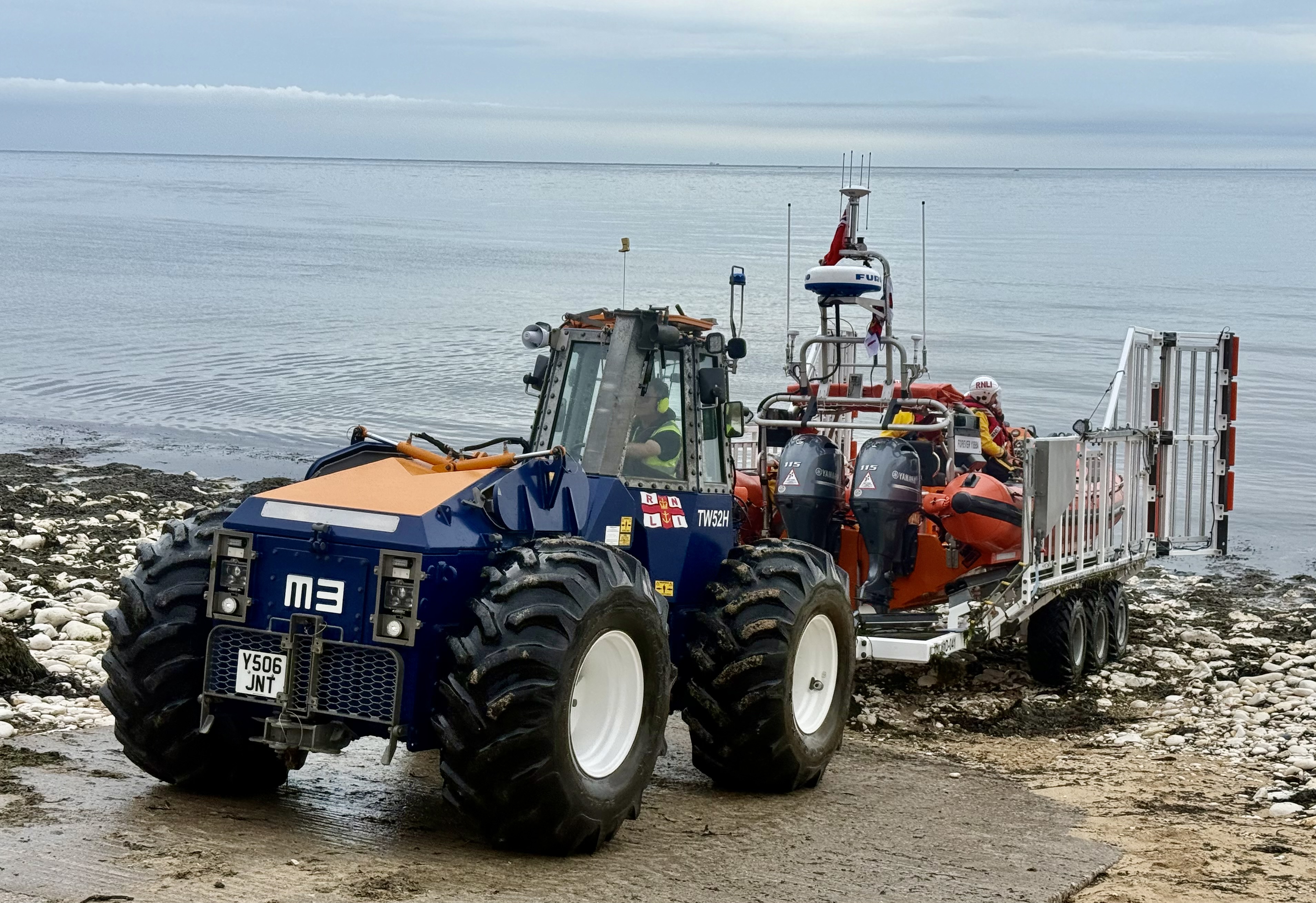 Lifeboat in carriage with tractor towing up the slipway