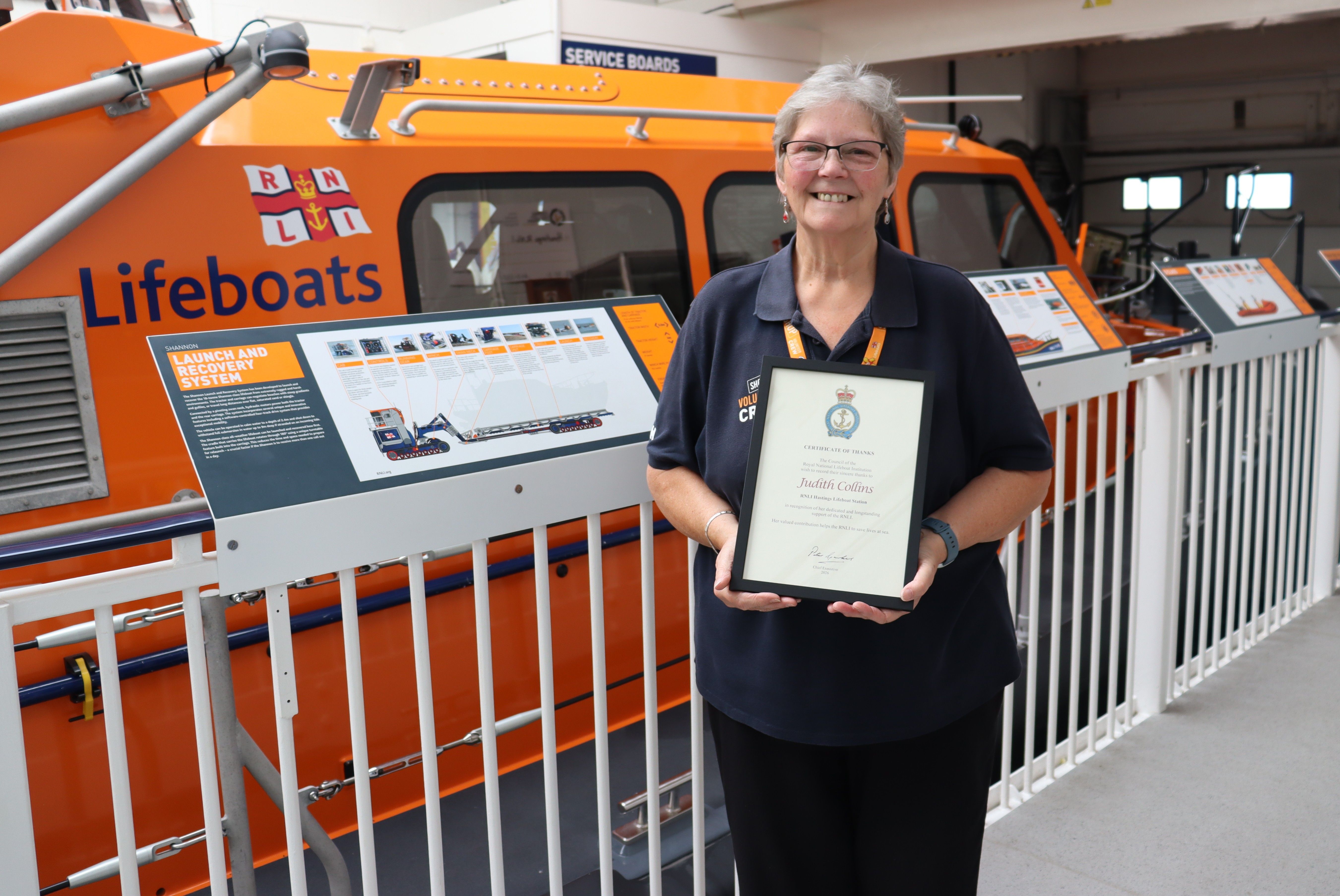 Judith Collins with her framed certificate of thanks standing in front of Hastings lifeboat RNLB Richard and Caroline Colton