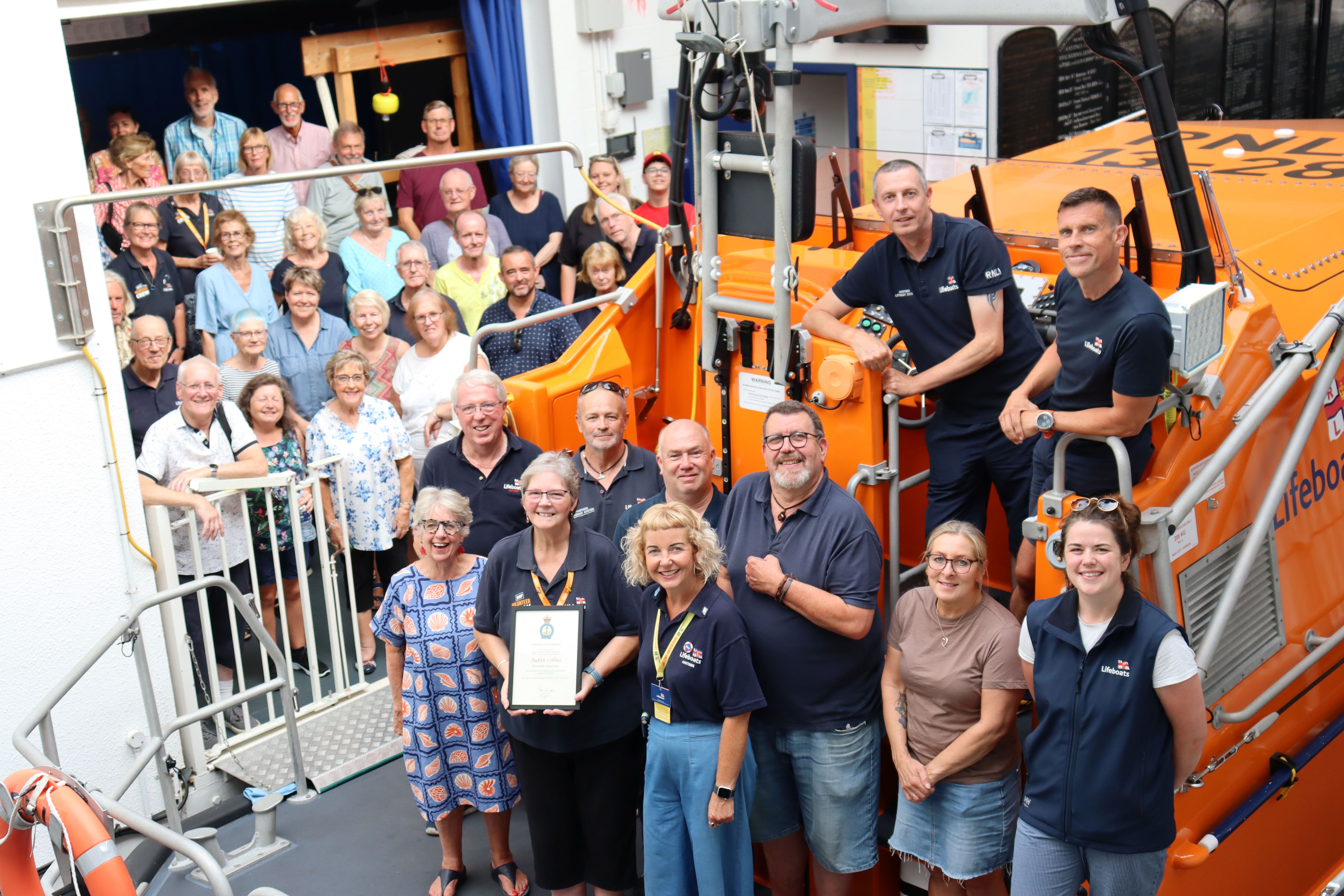 Judith Collins surrounded by dozens of RNLI volunteers standing on and behind Hastings lifeboat RNLB Richard and Caroline Colton