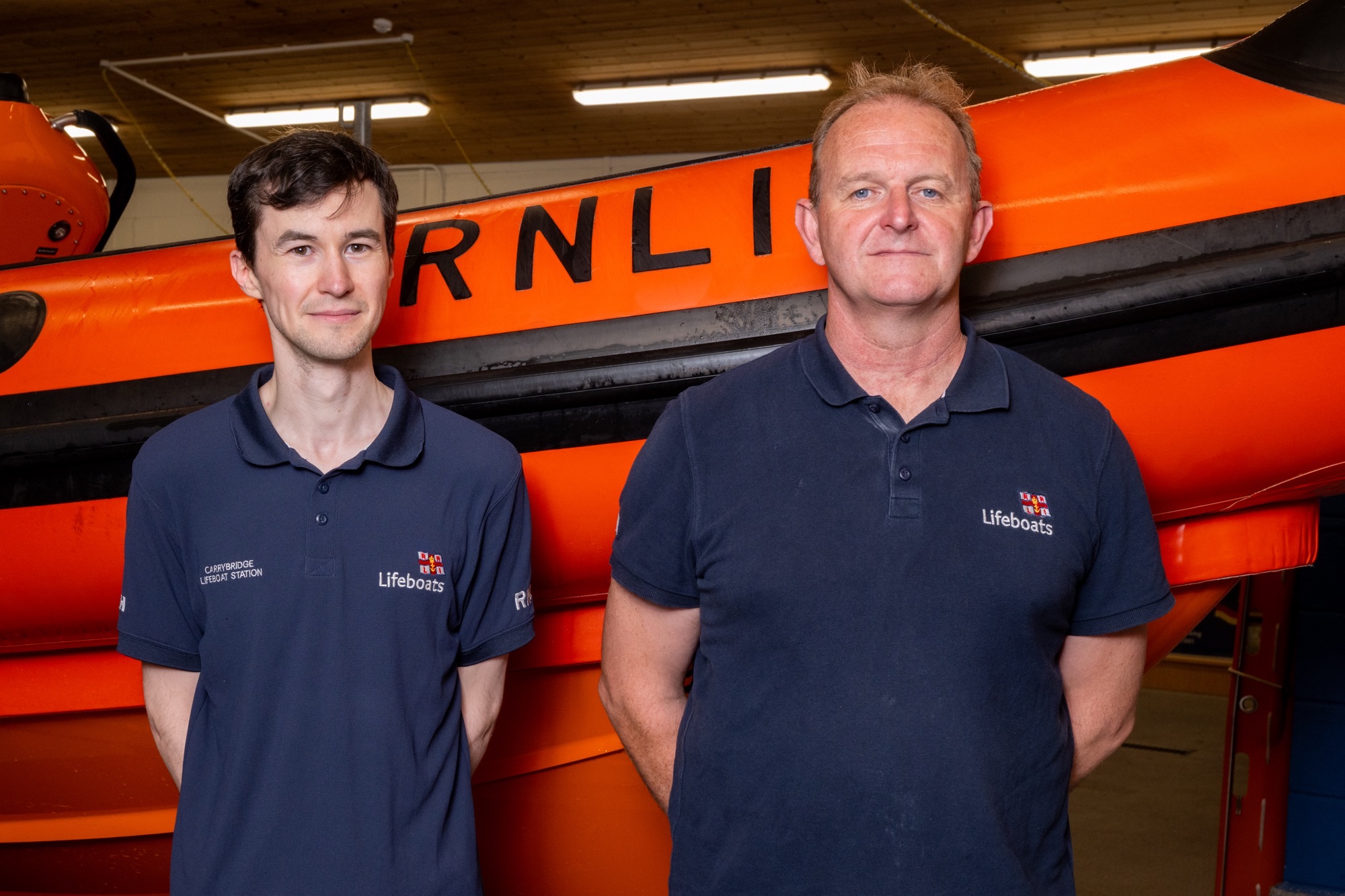 New helm, Matthew Nelson, standing beside Sean Ginnelly, Coastal Lifeboat Trainer, with the lifeboat in the background.