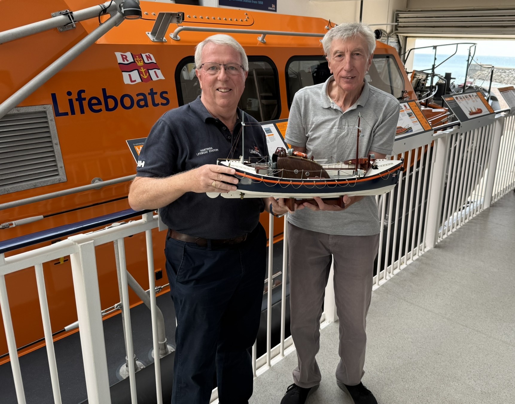 Paul Freathy and Bob Cakebread are holding the model of the MTC in front of Hastings' current Shannon lifeboat