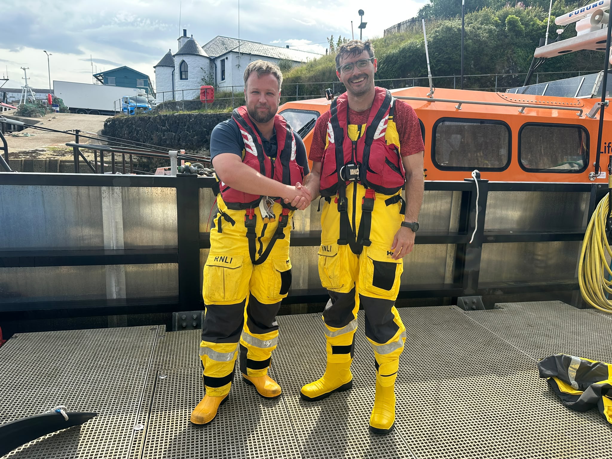 Tom and Tom shaking hands standing in the sunshine in front of Oban's Shannon class lifeboat, The Campbell-Watson