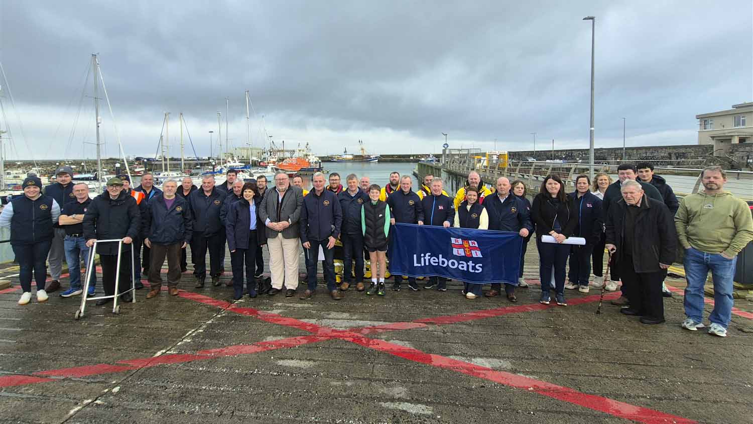 Group photo of fundraisers and crew members standing on the slip in Kilmore Quay with the lifeboat moored in the background