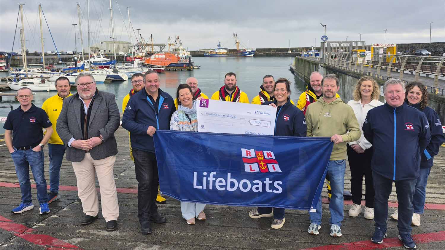 Group photo of 20 Dips in December fundraisers and crew members standing on the slip in Kilmore Quay with the lifeboat moored in the background