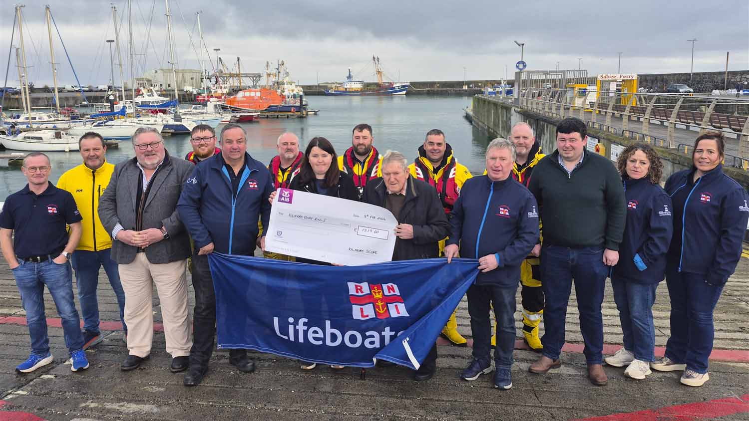 Group photo of Kilmore SCOPE members and crew members standing on the slip in Kilmore Quay with the lifeboat moored in the background