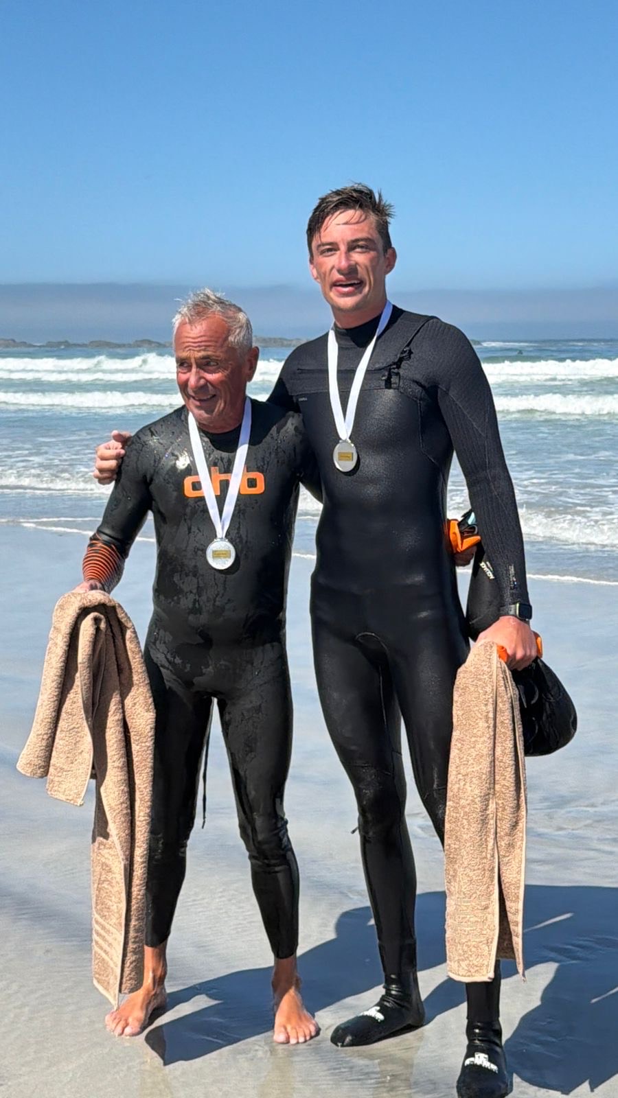 Richard (L) and his swim partner Aldo Scribante (R) ono the shoreline in wetsuits with medals around there necks.