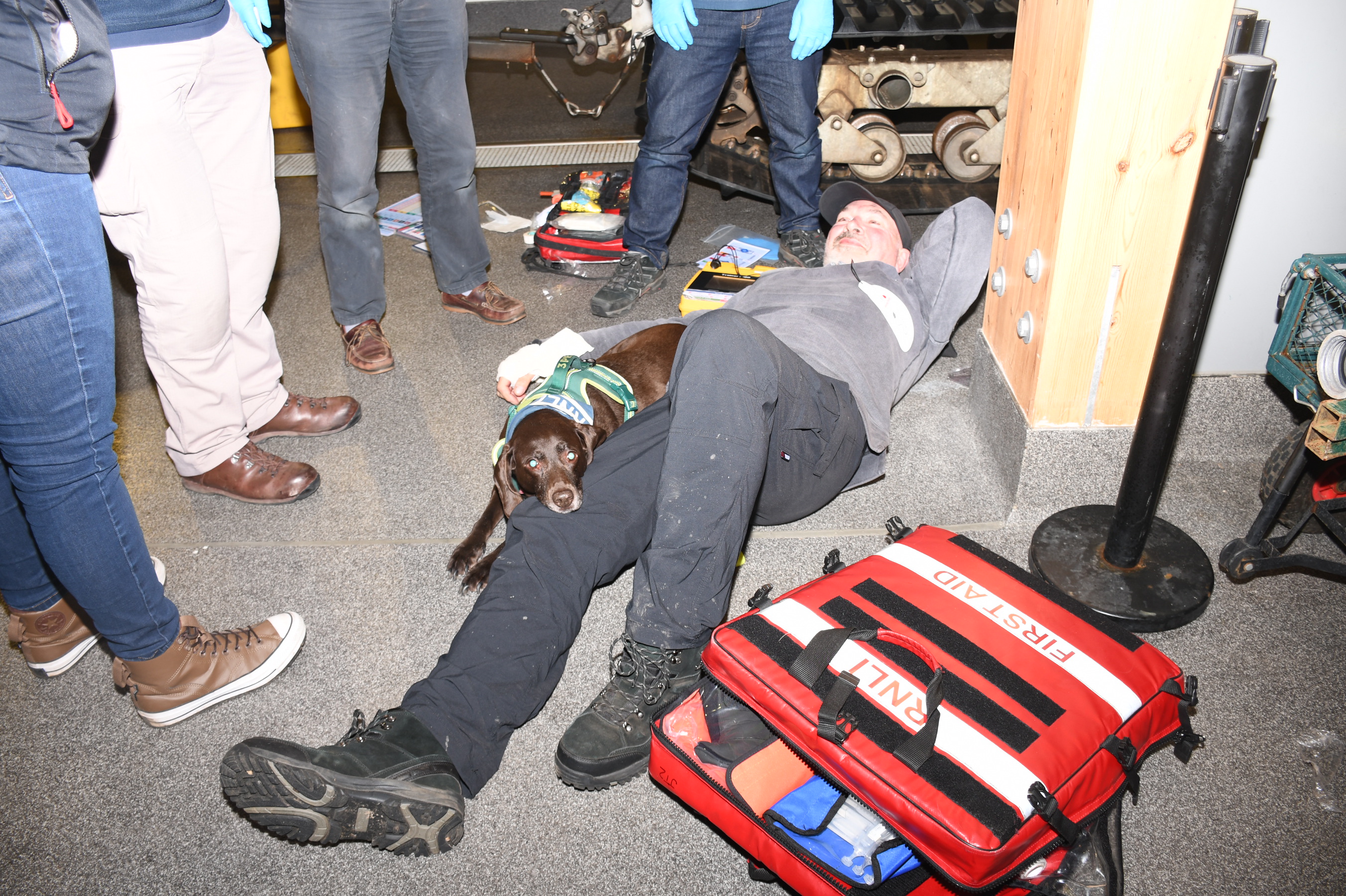 Wells RNLI crew member laying on the floor pretending to be ill in casualty care training with brown dog laid beside him