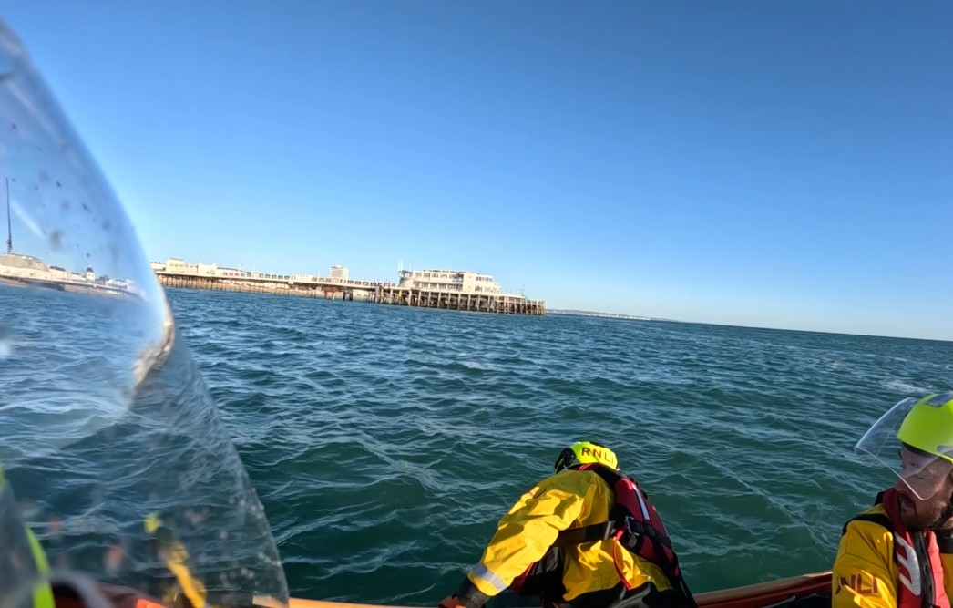 Crew member learning over side of d-class to pull casualty into boat.