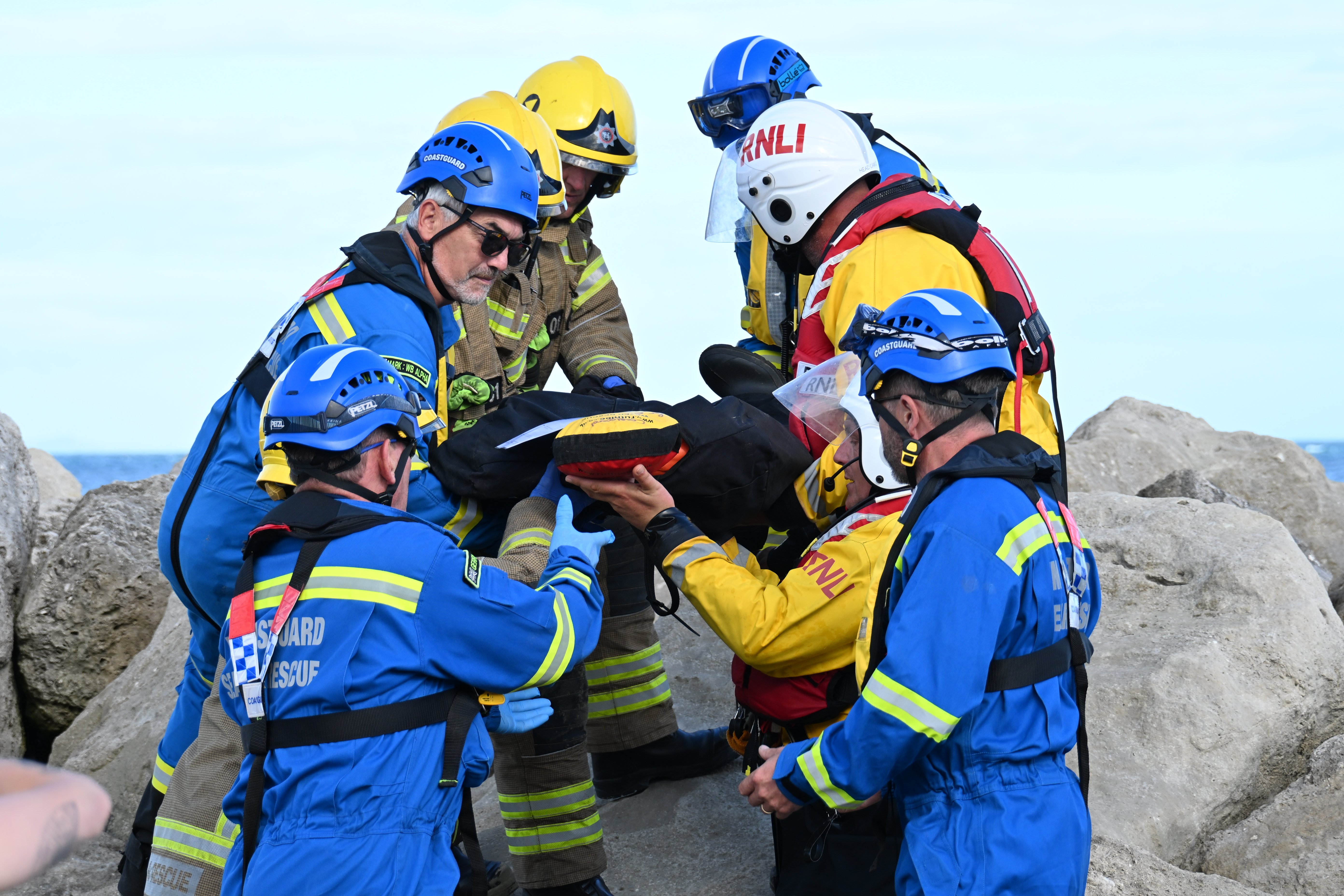 Eight men carrying a stretcher off rocks