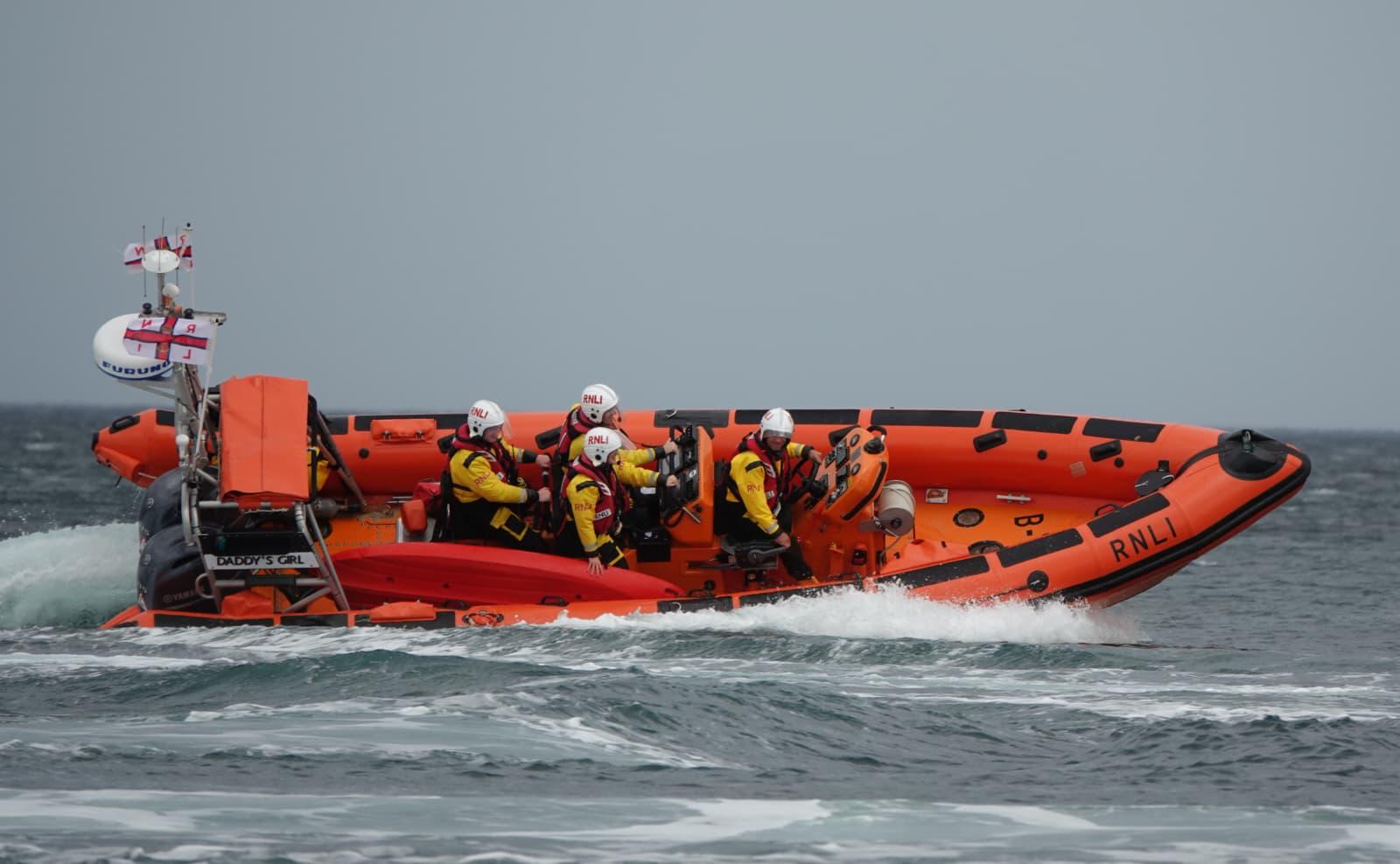 Orange lifeboat afloat on its side with four people onboard
