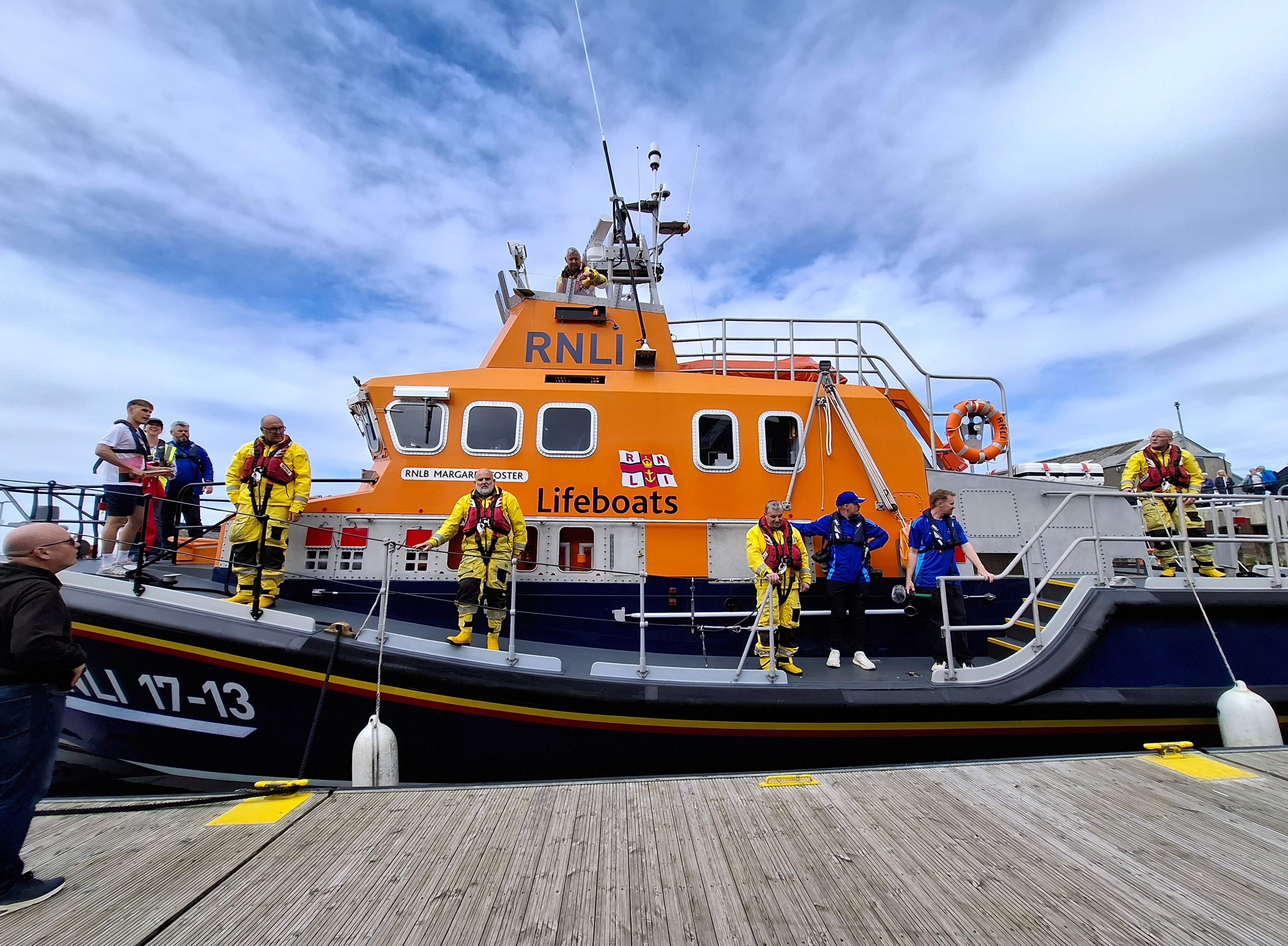 RNLI lifeboat with crew, young athlete and Team Scotland people in royal blue jackets.