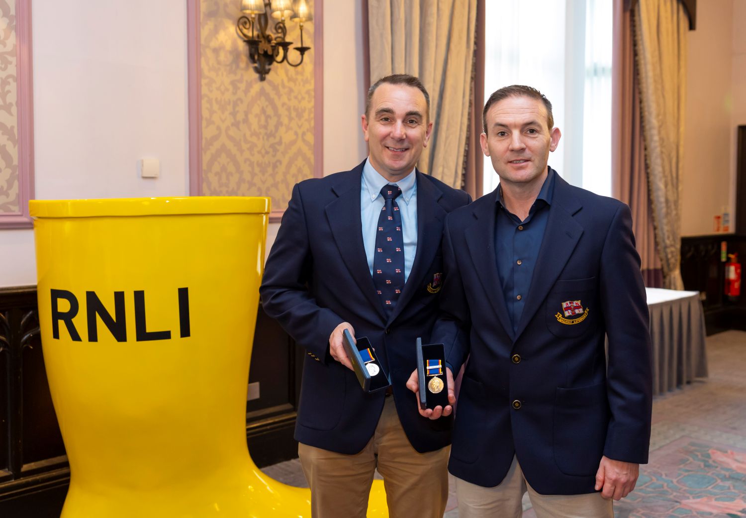Two crew inside a function room holding 30 year long service medals